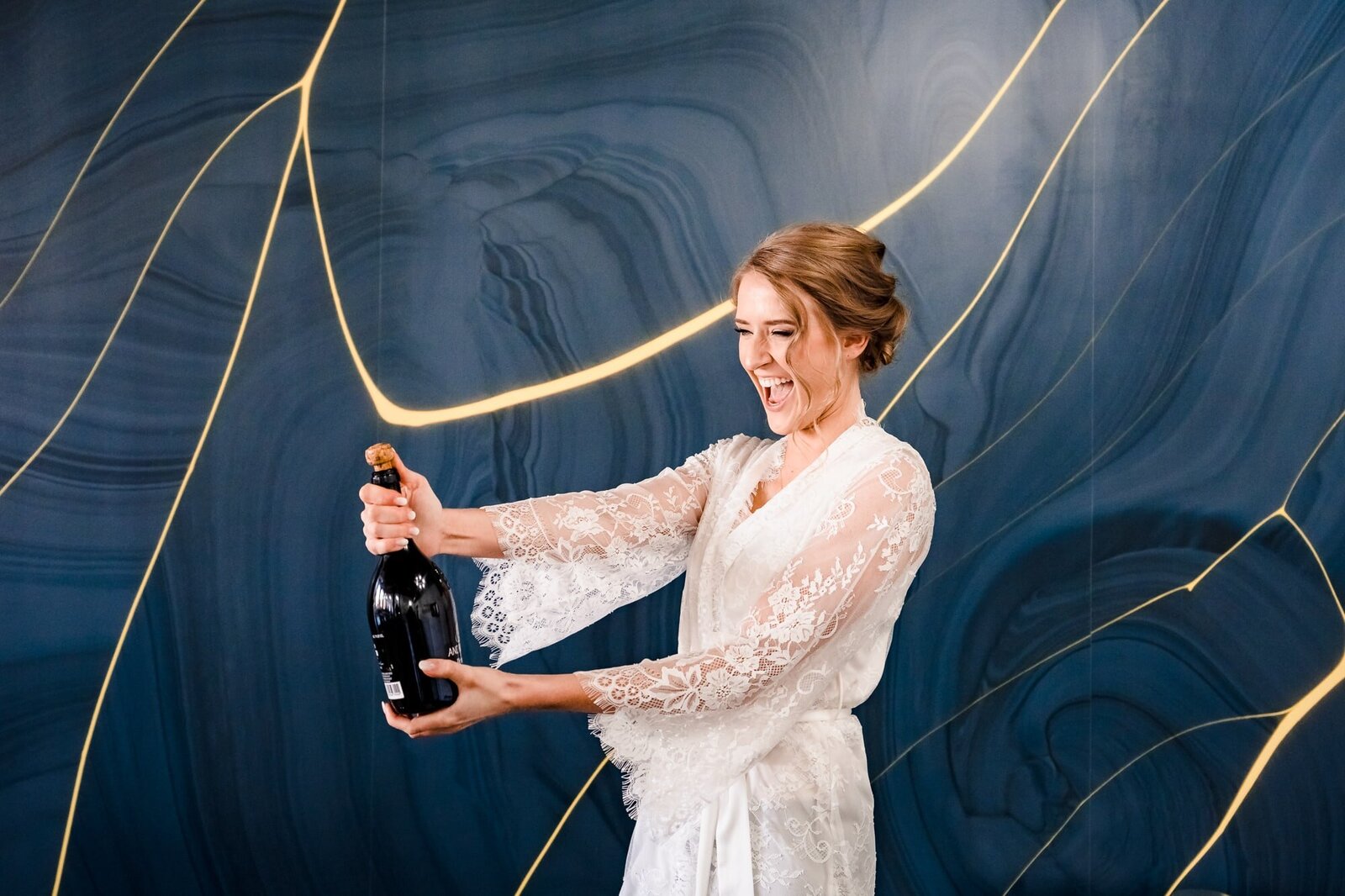 Woman in a white silk robe pops champagne on her wedding morning