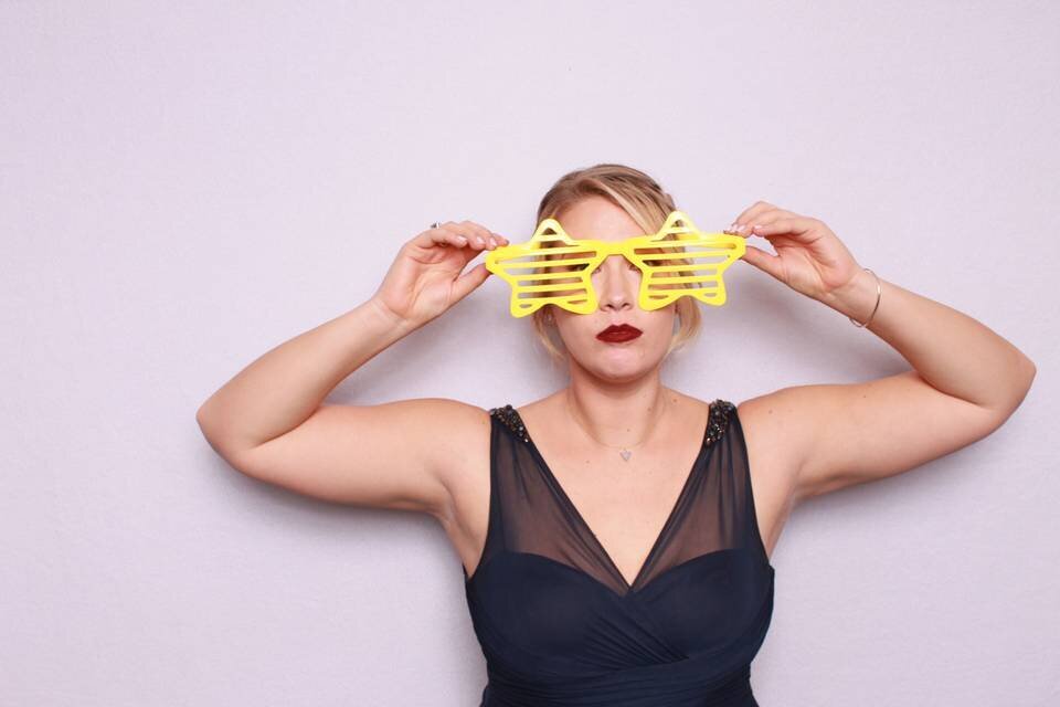 woman in black dress and silly star glasses in front of a pink backdrop in a photo booth rental in philadelphia