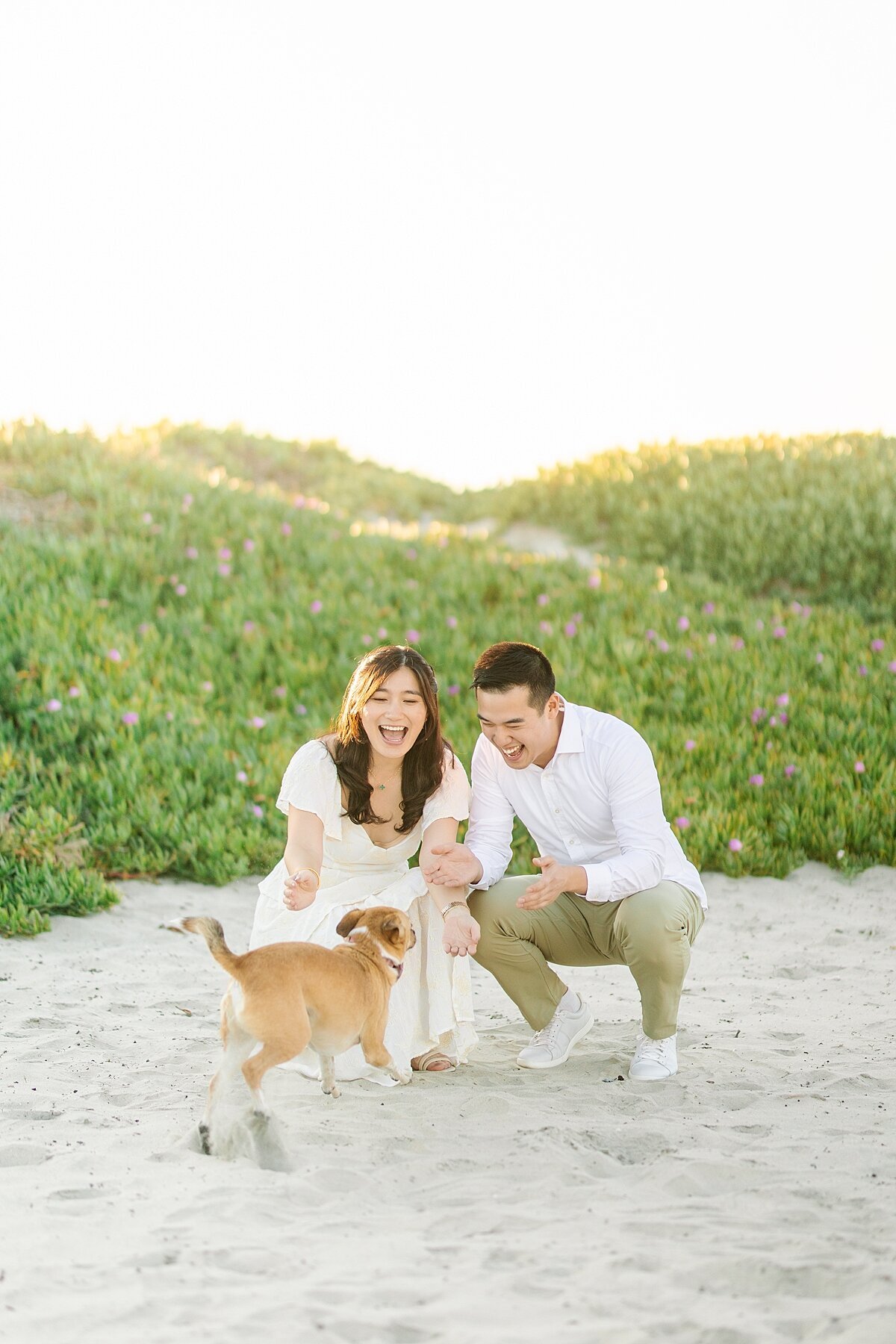 Engaged couple playing with their dog on the sand dunes at Coronado Beach.