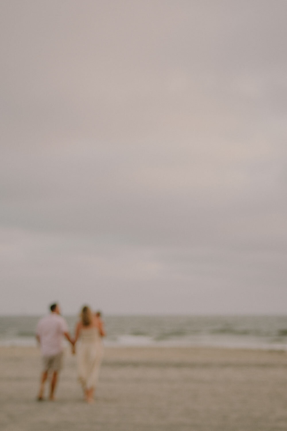 Blurred couple walking on the beach with baby at sunset