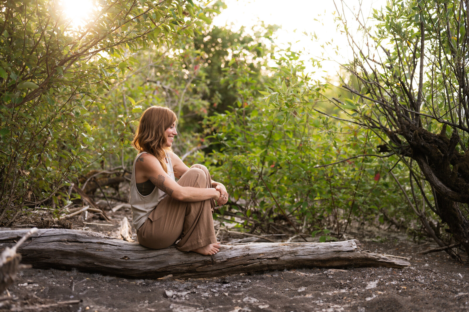 yoga teacher sitting on a log with green trees behind