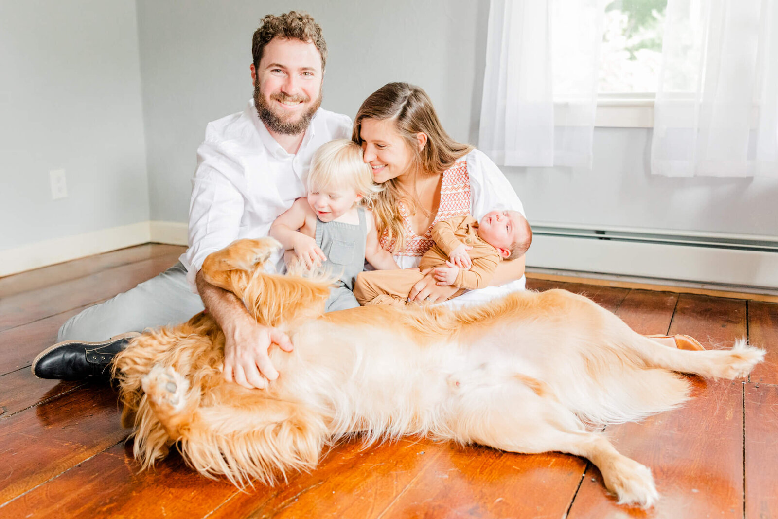 A golden retriever spreads out all his limbs to ask for a belly rub with the family smiling in the background