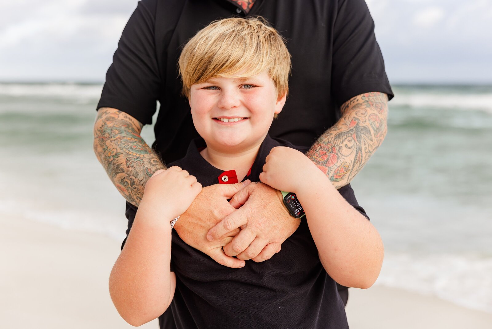 Dad with tattooed arms embracing son prompt during Pensacola Beach trip family photo session by Jennifer Beal Photography