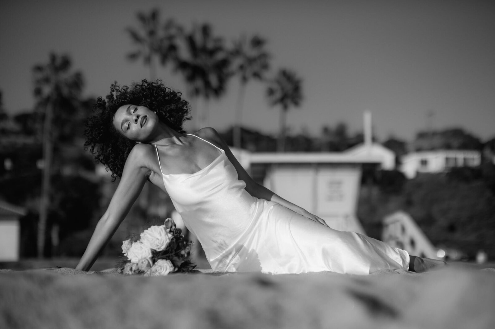 Bride lays on the beach with eyes closed.