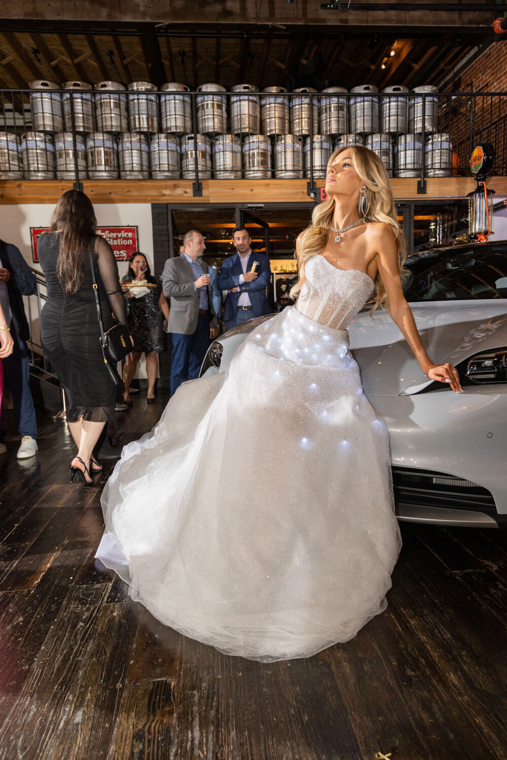 Woman in a sparkling light-up gown leaning against a silver car
