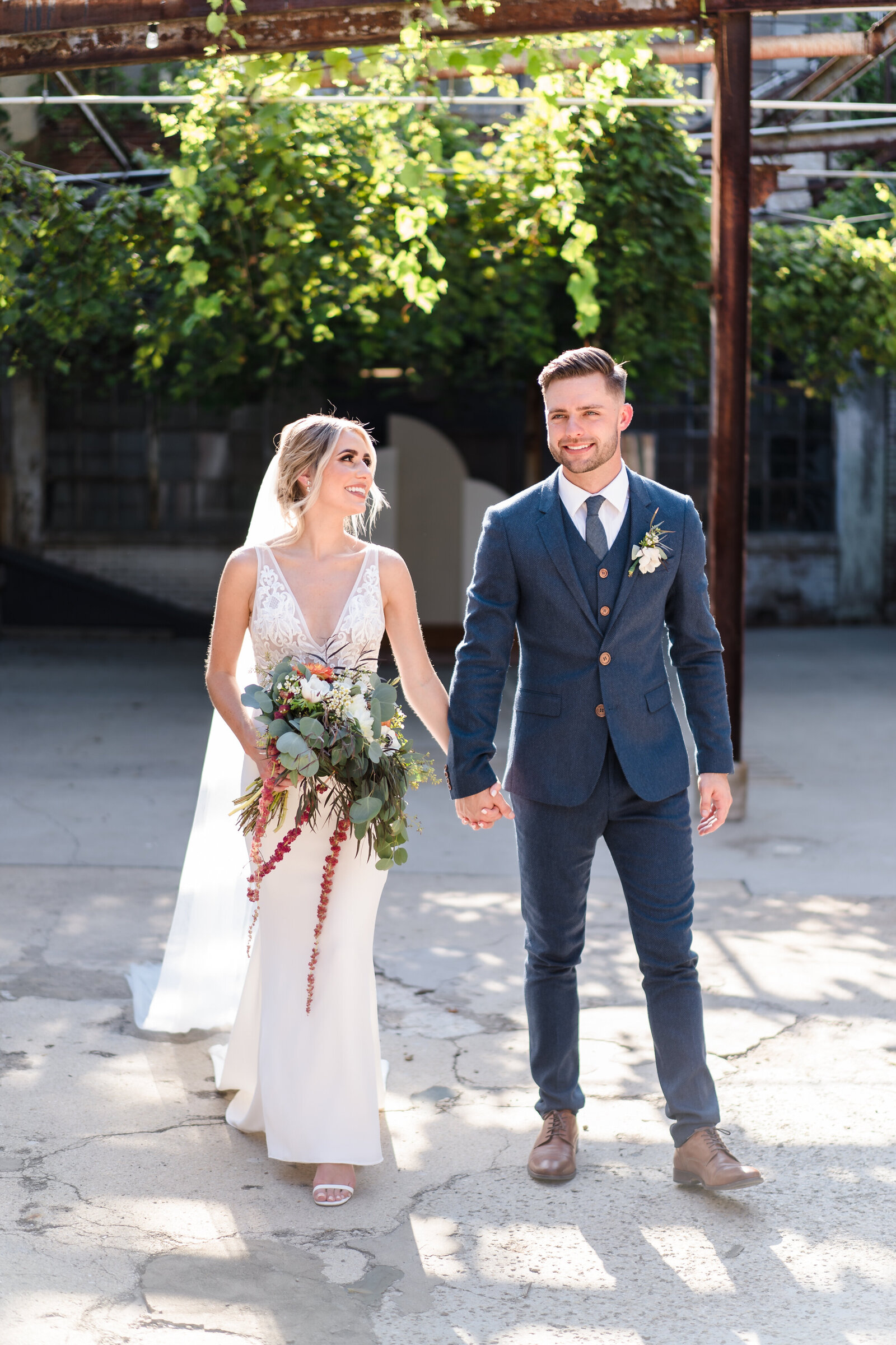 A bride and groom hold hands and smile as they walk in the courtyard at Strongwater