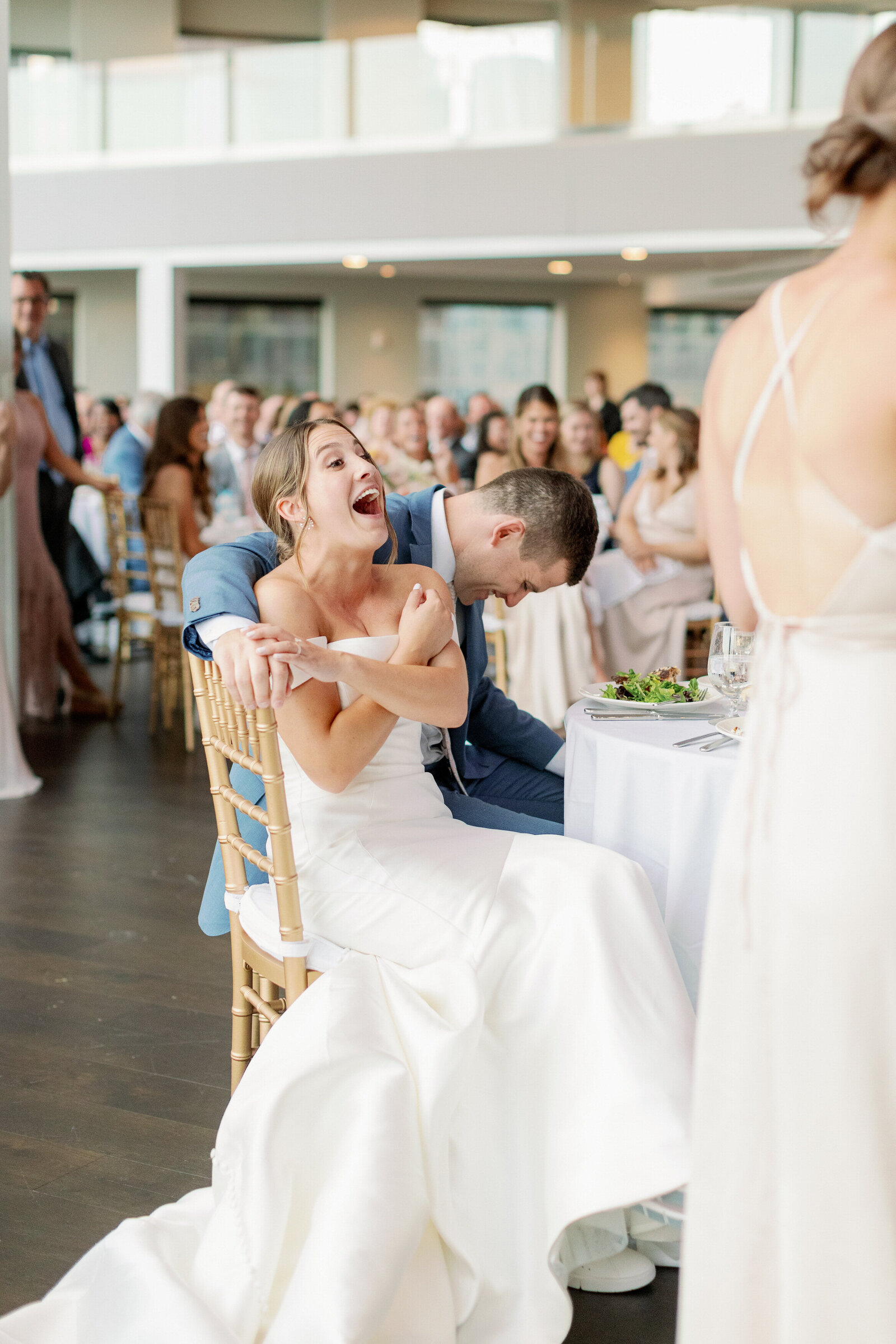 Bride laughing as she sits down at her wedding reception.