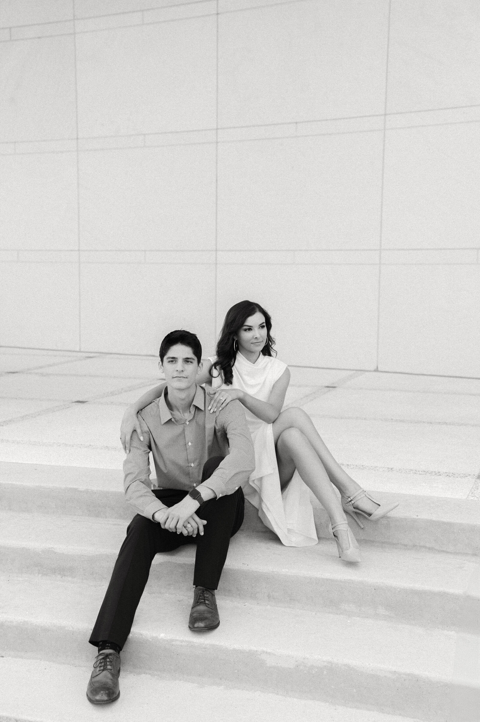 black and white engagement session photo at texas a and m university. man and woman sitting on the steps at TAMU, looking into the distance, by tara paige wedding photographer