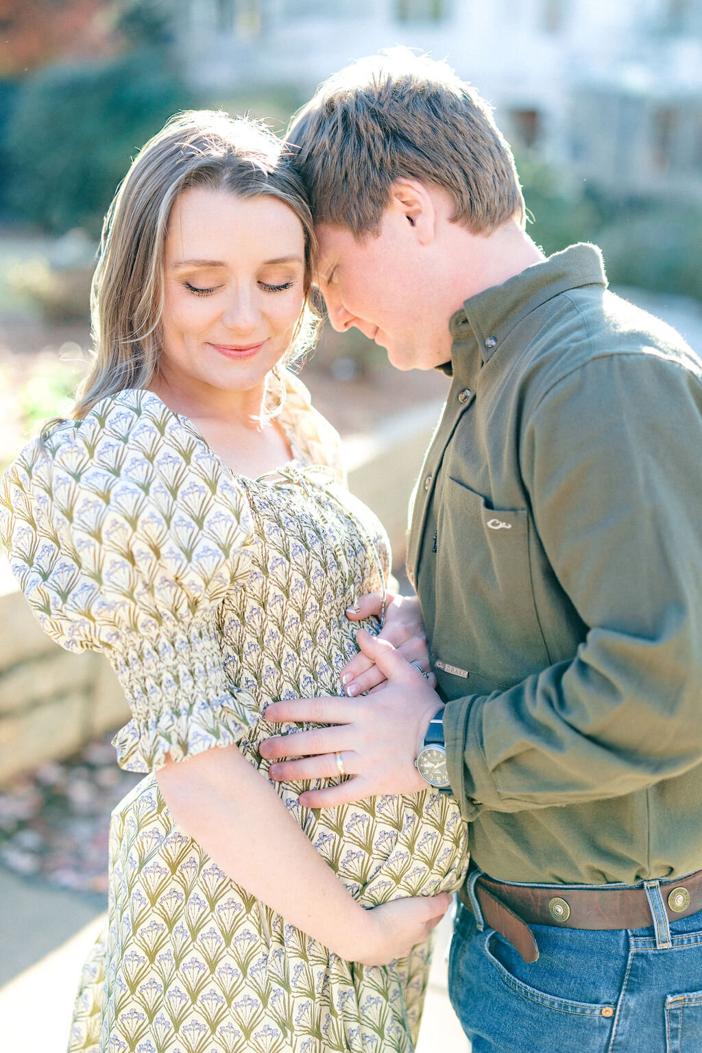 Woman in green patterned dress holds baby bump with husband