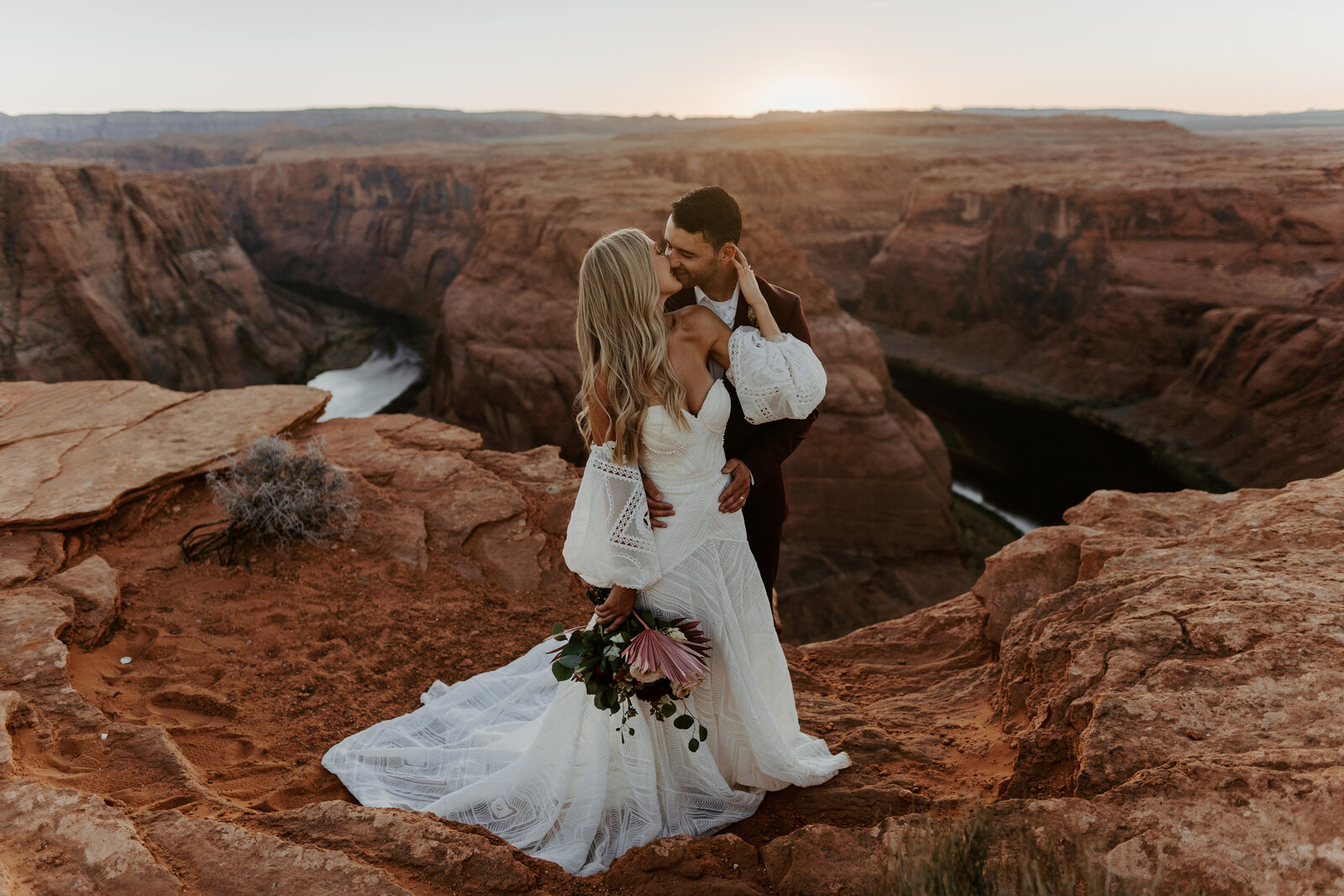 Bride and groom in boho wedding attire kissing on the cliffs in front of Horseshoe Bend, Arizona