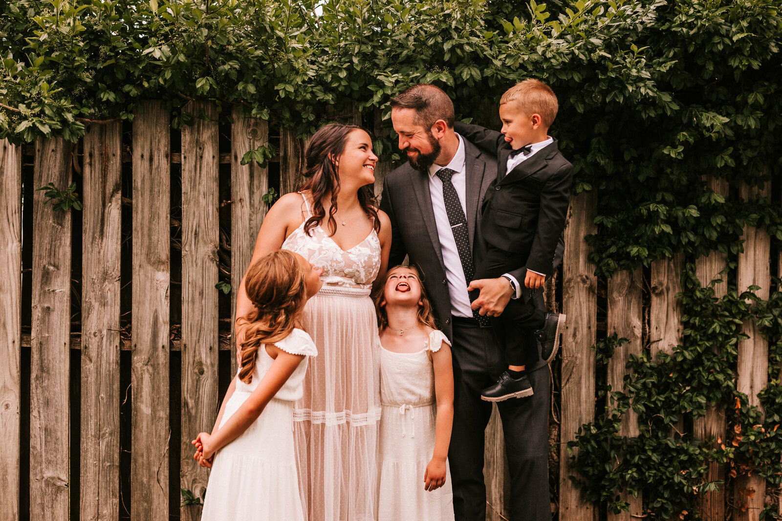 blended family at small wedding outside standing and looking at each other while laughing