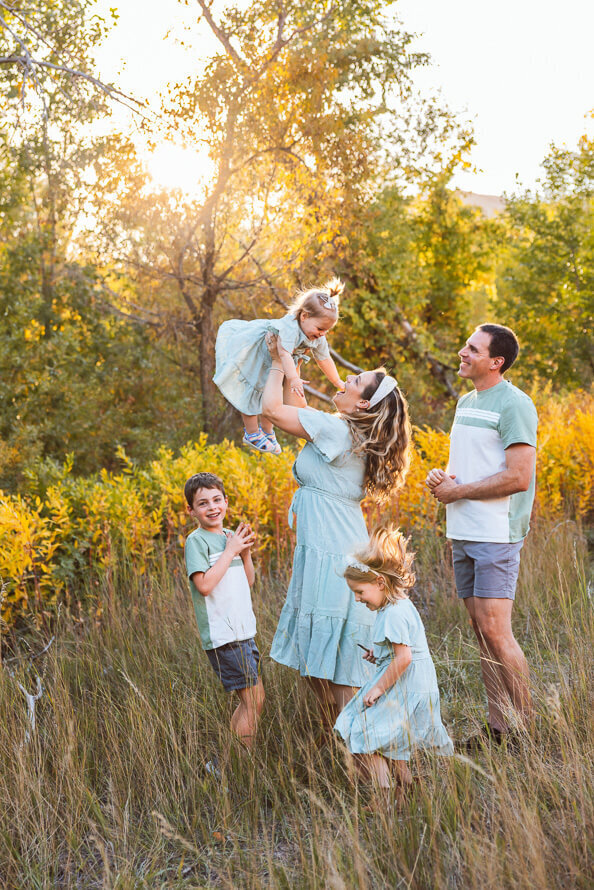 Family dressed in blue dances in the yellow grass and trees in a field near Red Rocks Ampitheatre.