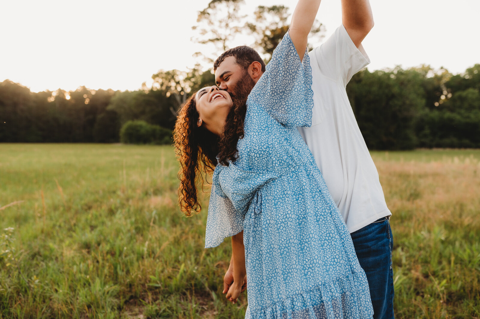 woman in a blue flowy dress dances with her fiance in an open field in little rock ar for their engagement photos