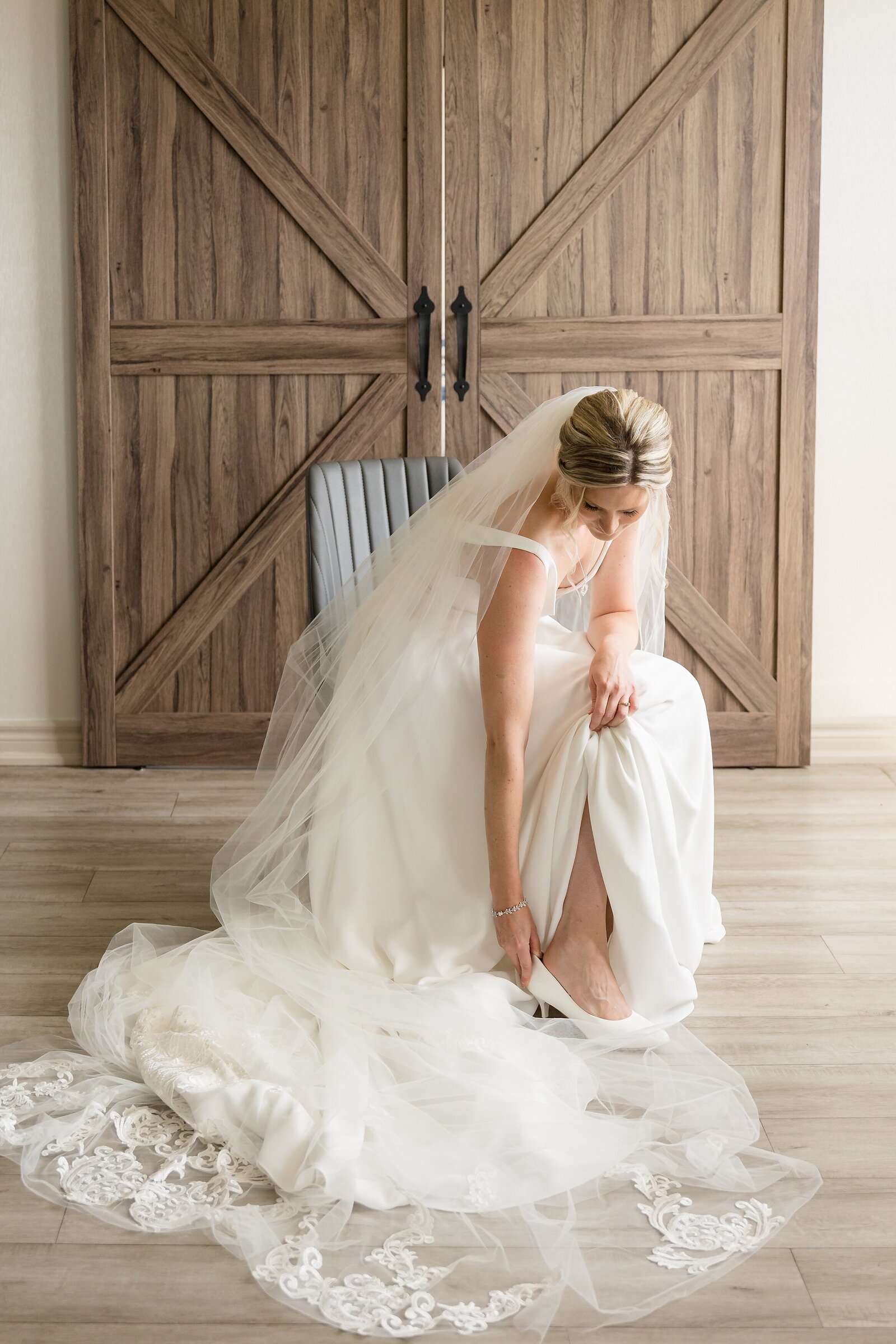 Stunning-bride-putting-on-her-wedding-shoes-in-front-of-sliding-barn-doors-at-the-park-hotel