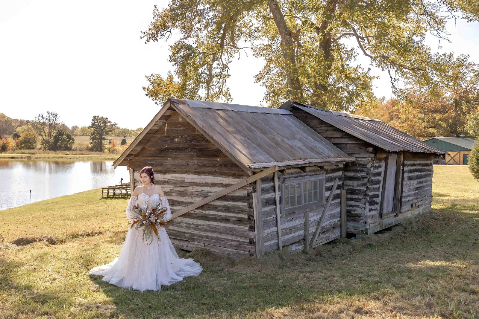 Bride posing gracefully in front of a rustic wooden cabin by a serene pond, showcasing a blend of elegance and nature in her wedding attire in Apex, North Carolina.