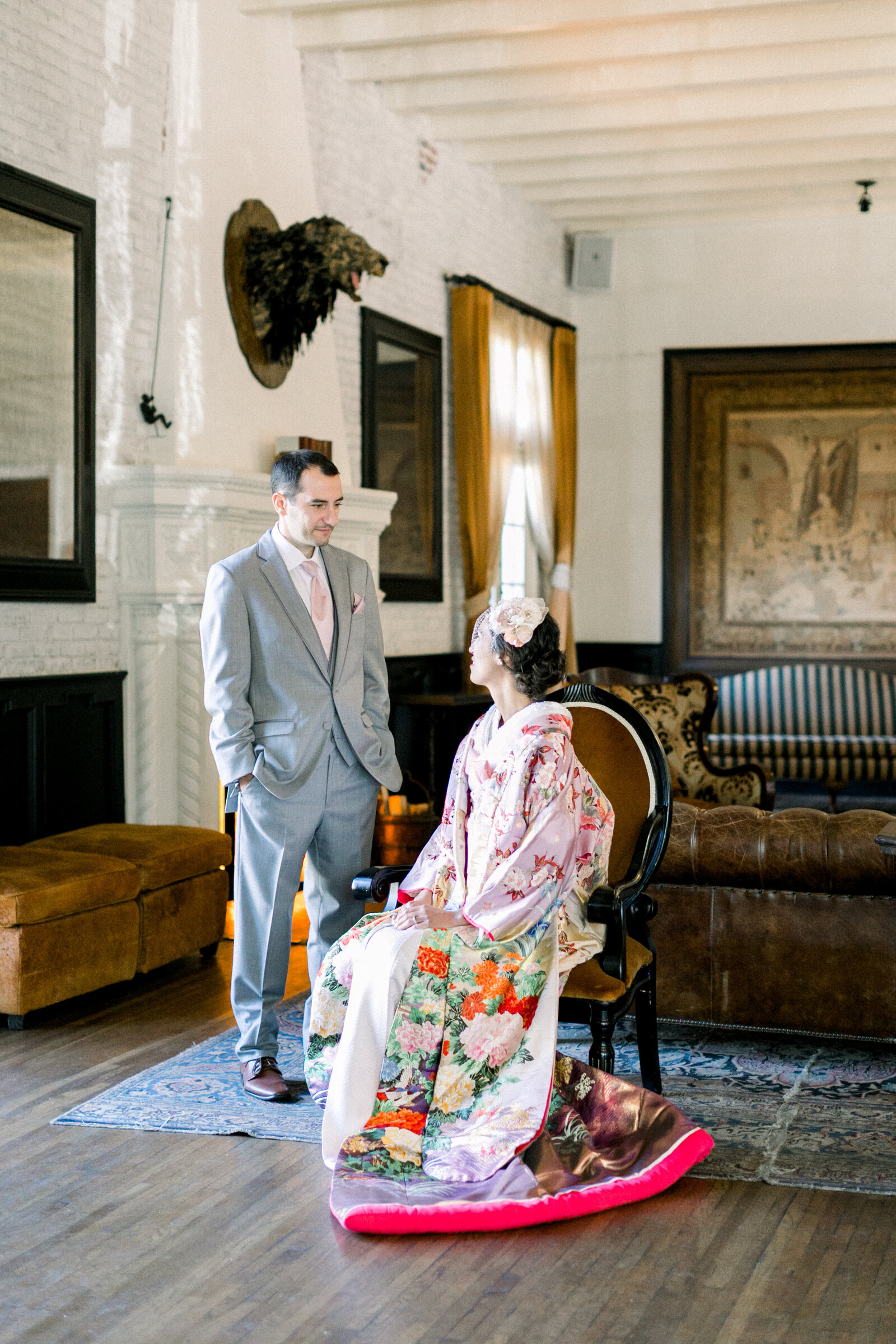 Bride in soft pink floral uchikake wedding kimono seated in vintage lounge with groom in light grey suit at The Ebell Club Long Beach, ideal for kimono rental in Los Angeles | ロサンゼルスThe Ebell Club Long Beachクラシックラウンジで淡いピンク色打掛花嫁とライトグレースーツ新郎の着物レンタル和婚ポートレート