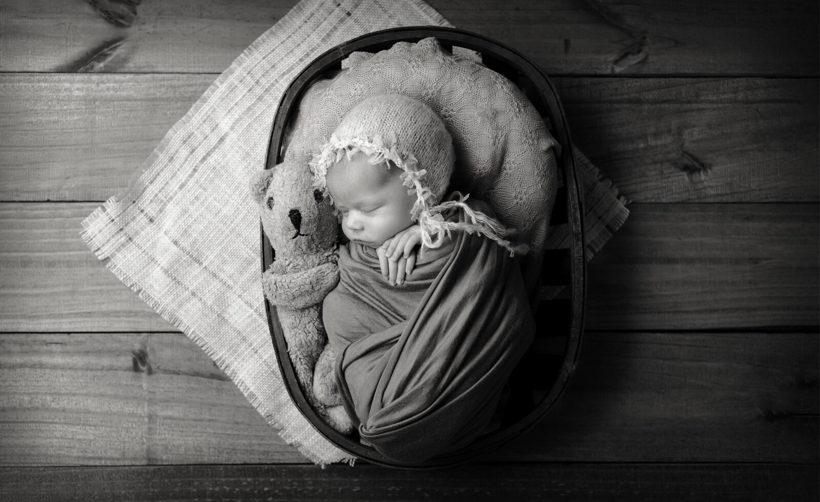 black and white newborn in a basket with teddy