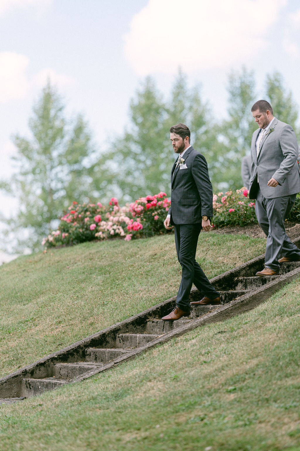 groom and best man descending stone steps with rose garden in the background