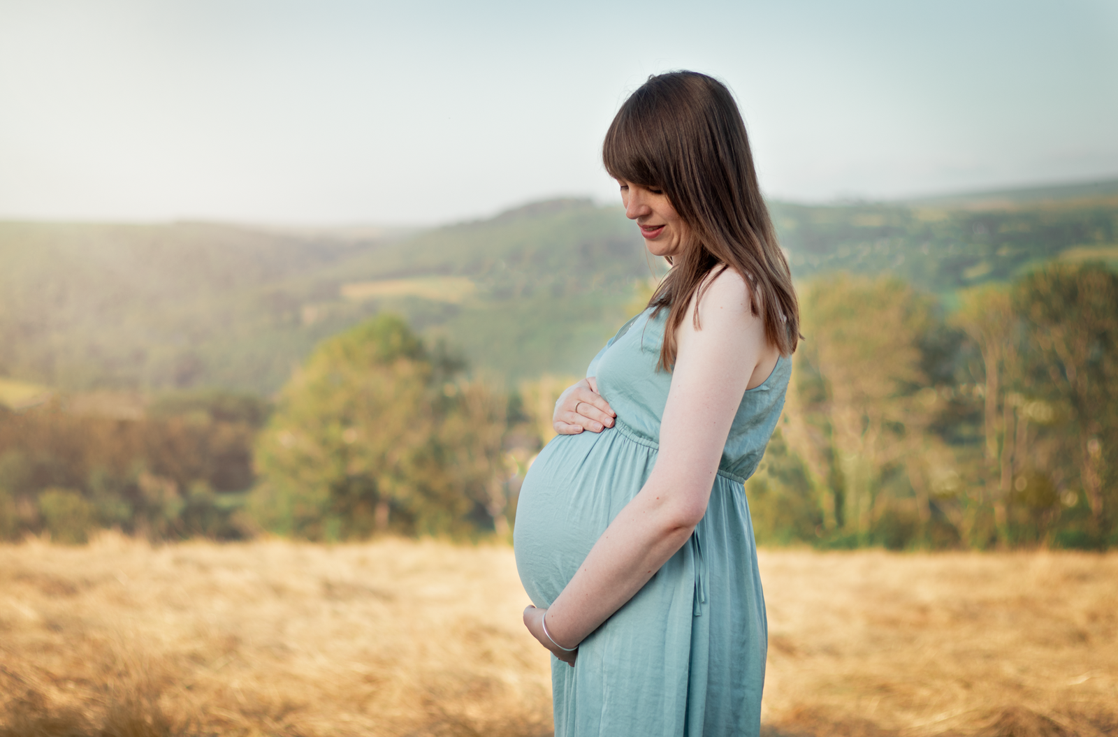 Lady stands in field holding her baby bump for outdoor maternity portraits