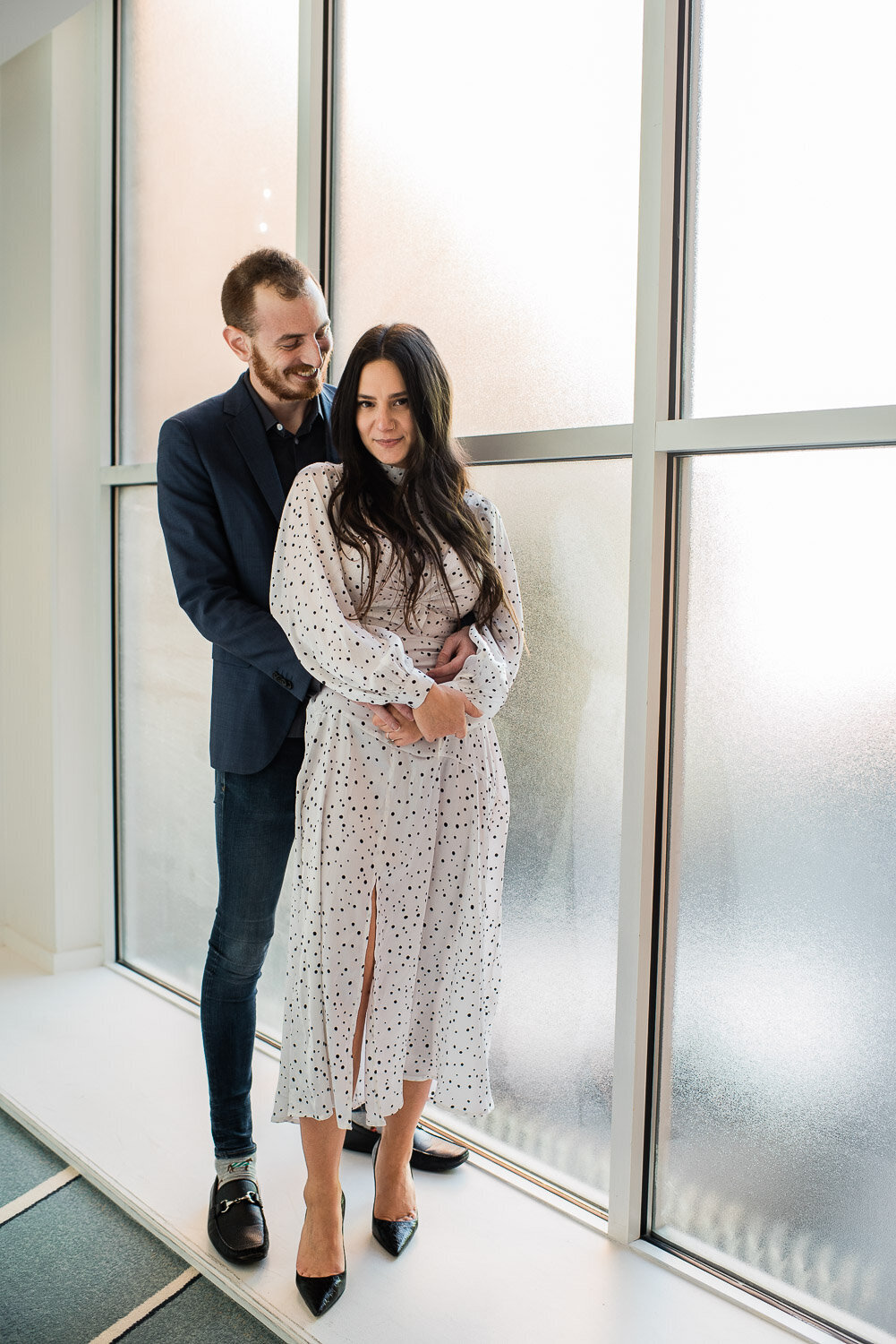 couple embrace in front of large window indoors