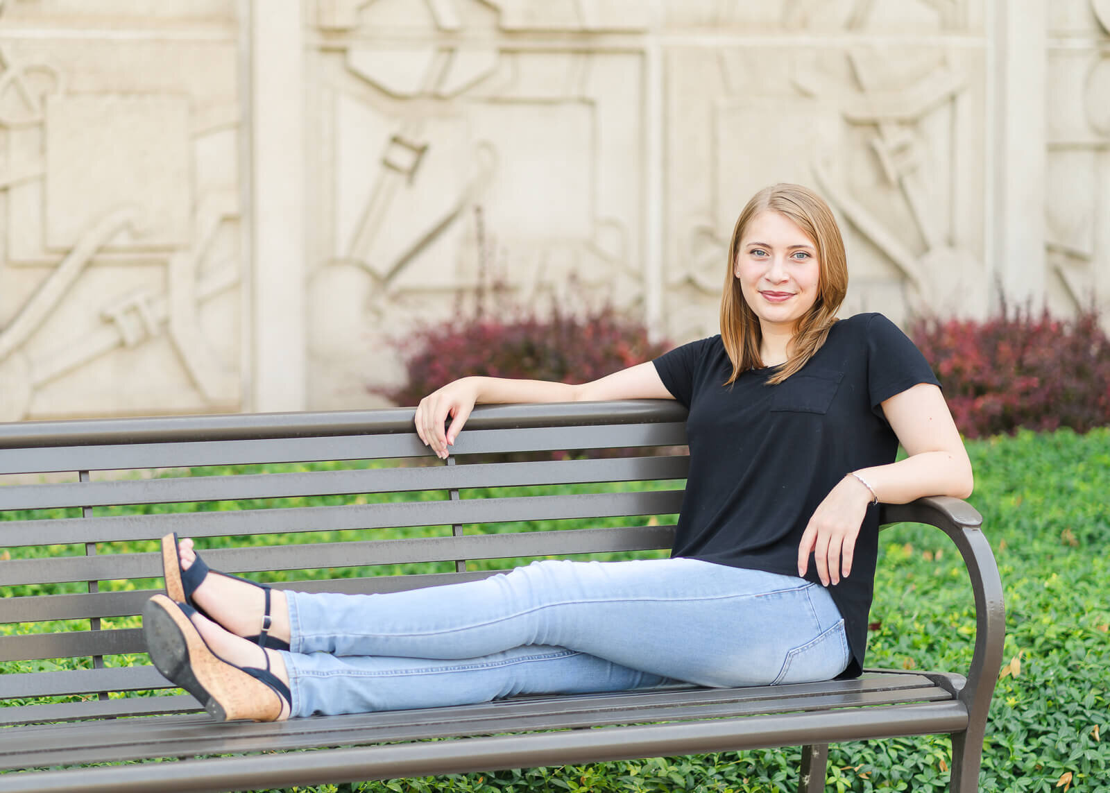 a high school senior girl wearing a black t-shirt and light blue jeans sits with her feet up on a bench at BYU in Provo
