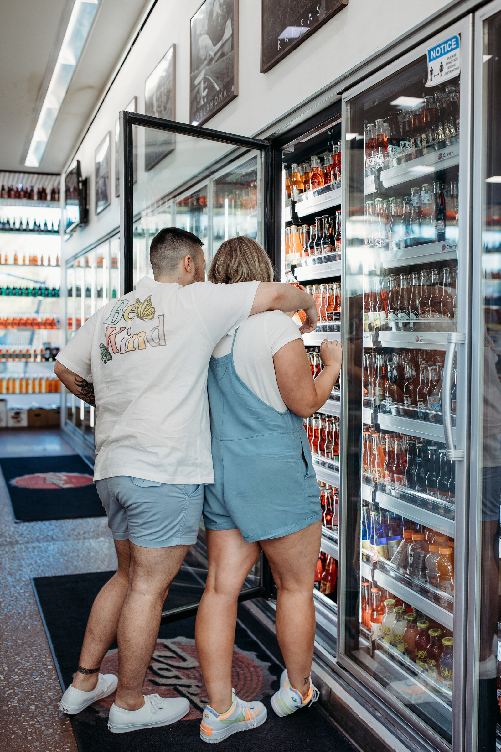A couple in summer attire leans into a refrigerator filled with colorful beverages