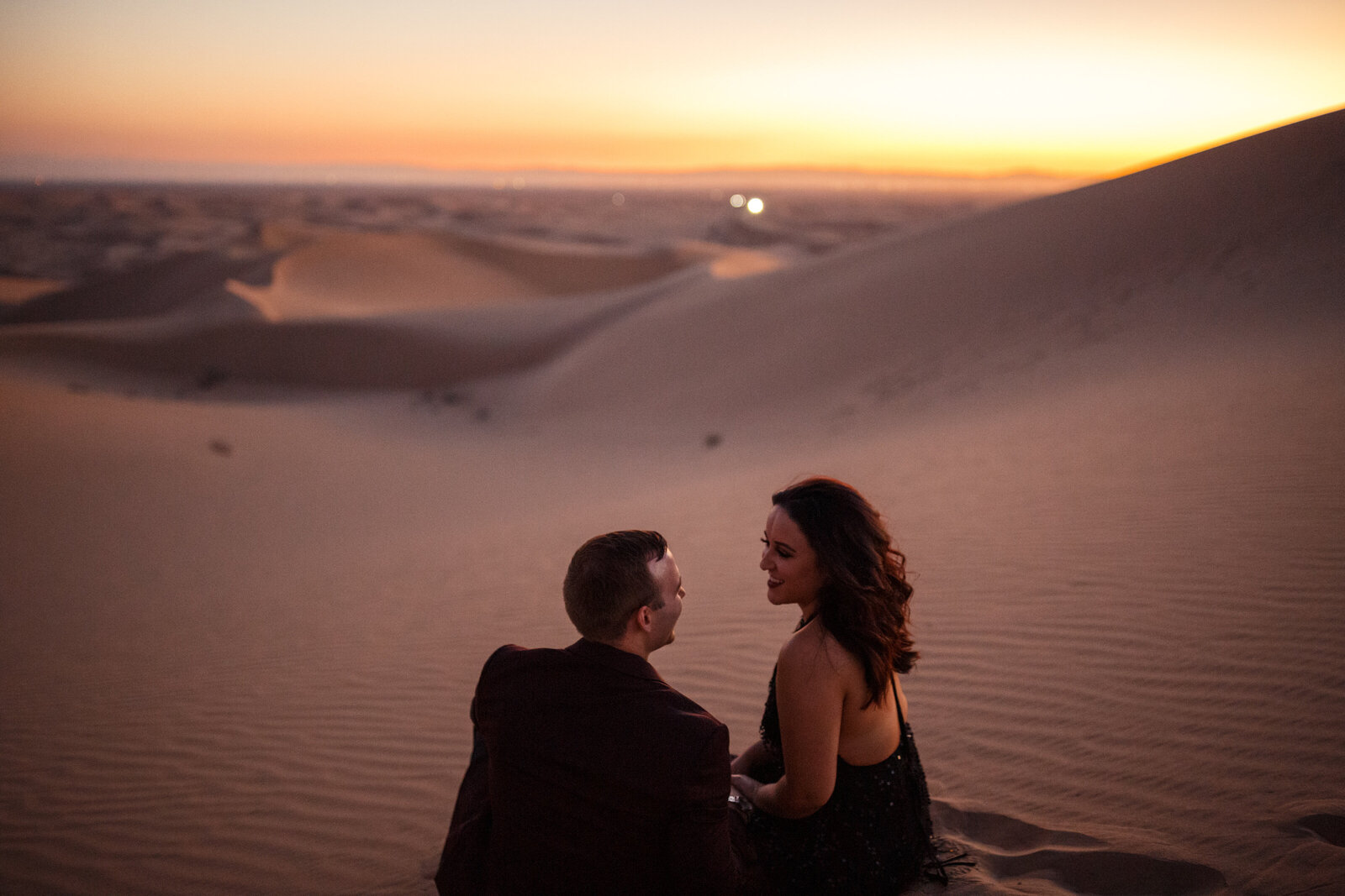 bride and groom sitting at the top of glamis sand dunes