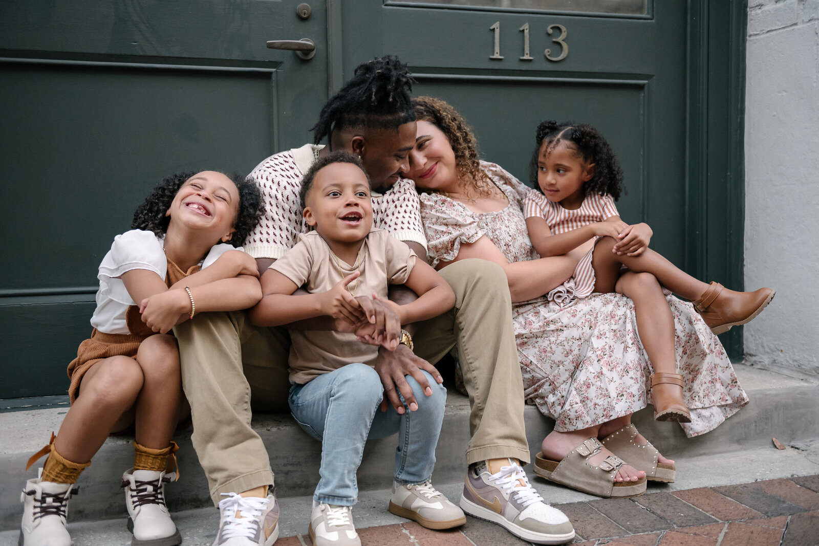 Happy family of five sitting on a doorstep, sharing a joyful moment during an outdoor lifestyle photoshoot. Captured by FDRPhotography in New Orleans, LA showcasing candid family connection and love.
