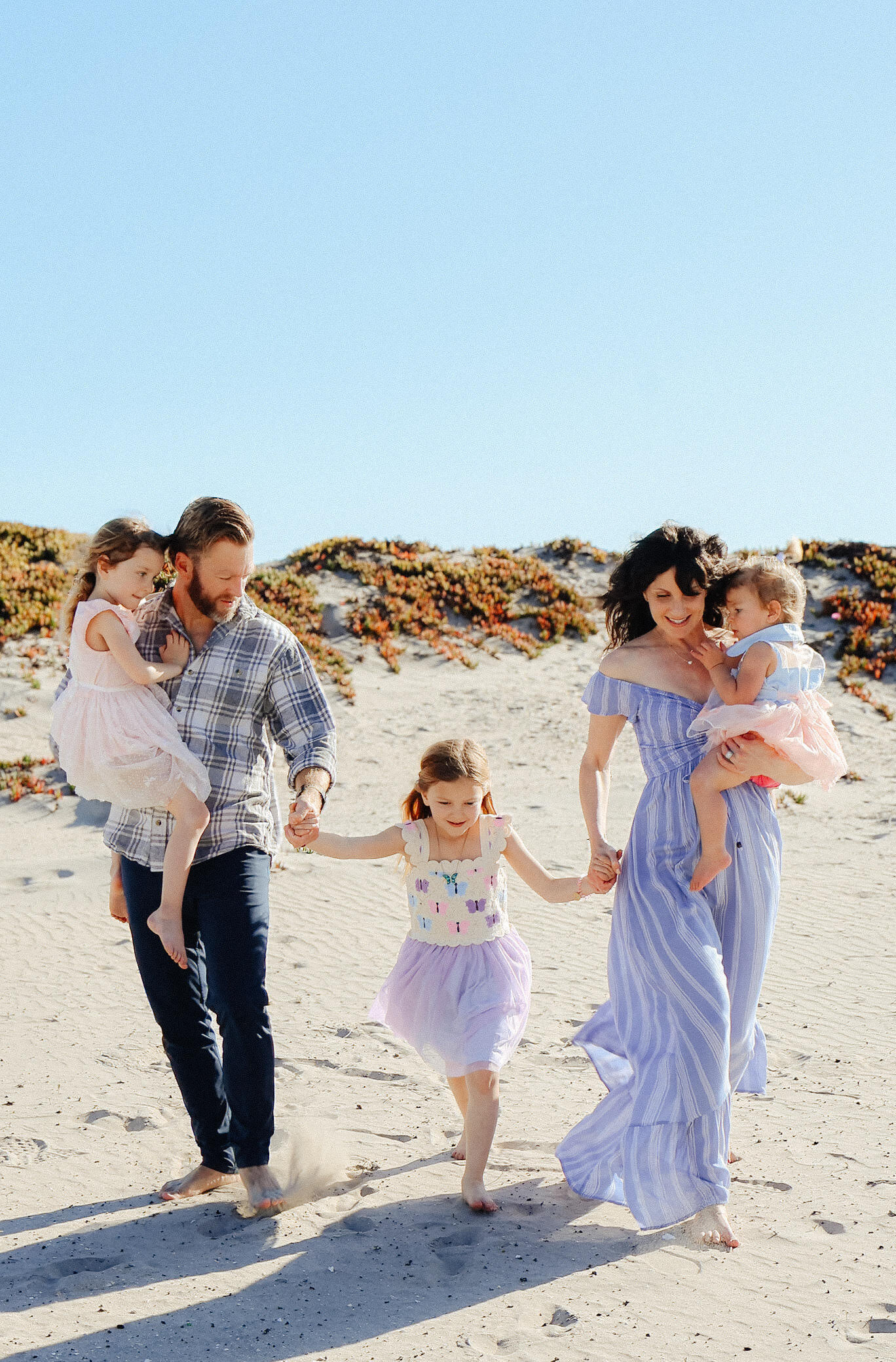 A family strolls along the beach, enjoying time together with their children, captured by a family photographer.