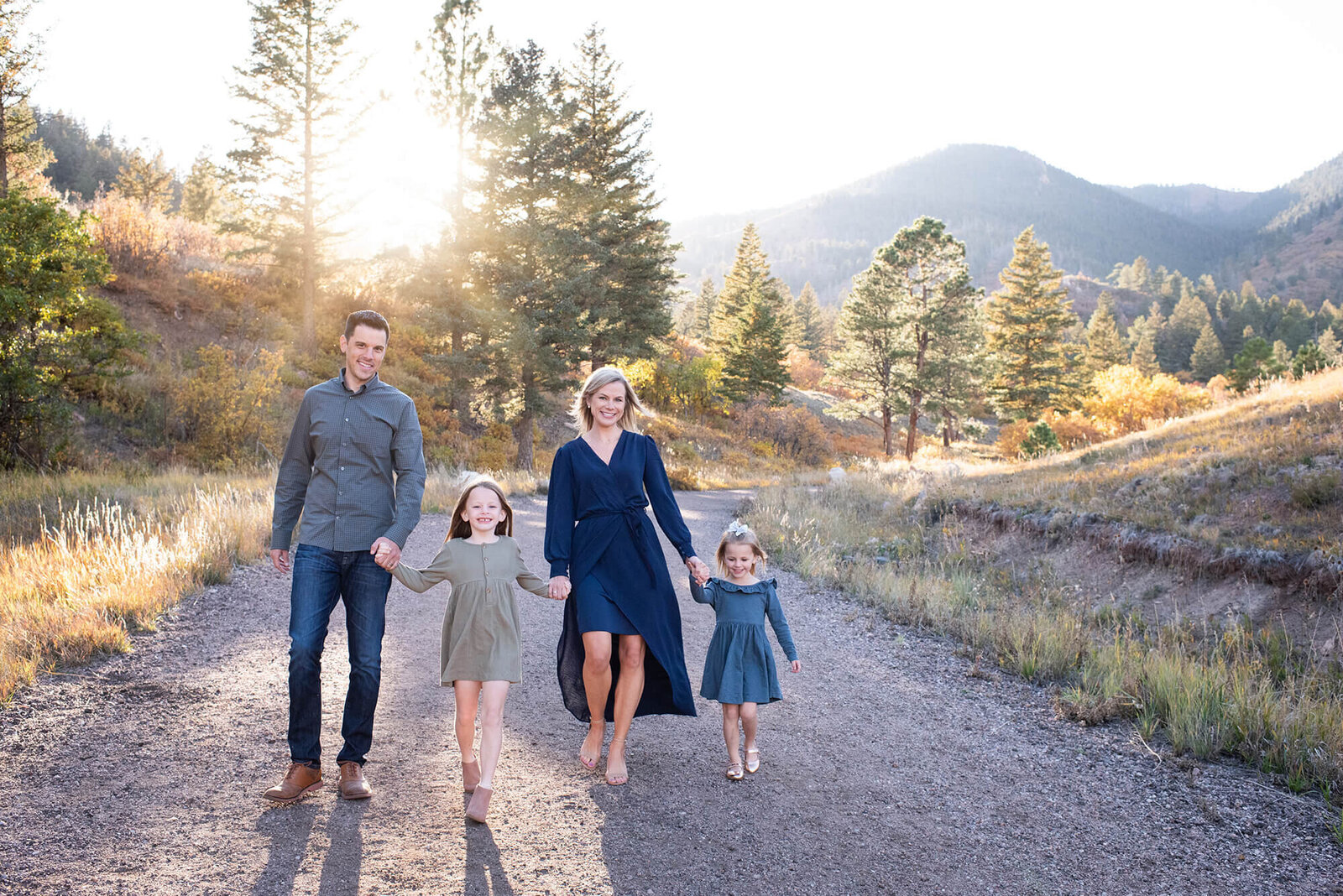A family of 4 with 2 toddlers happily walk down a trail at sunset holding hands
