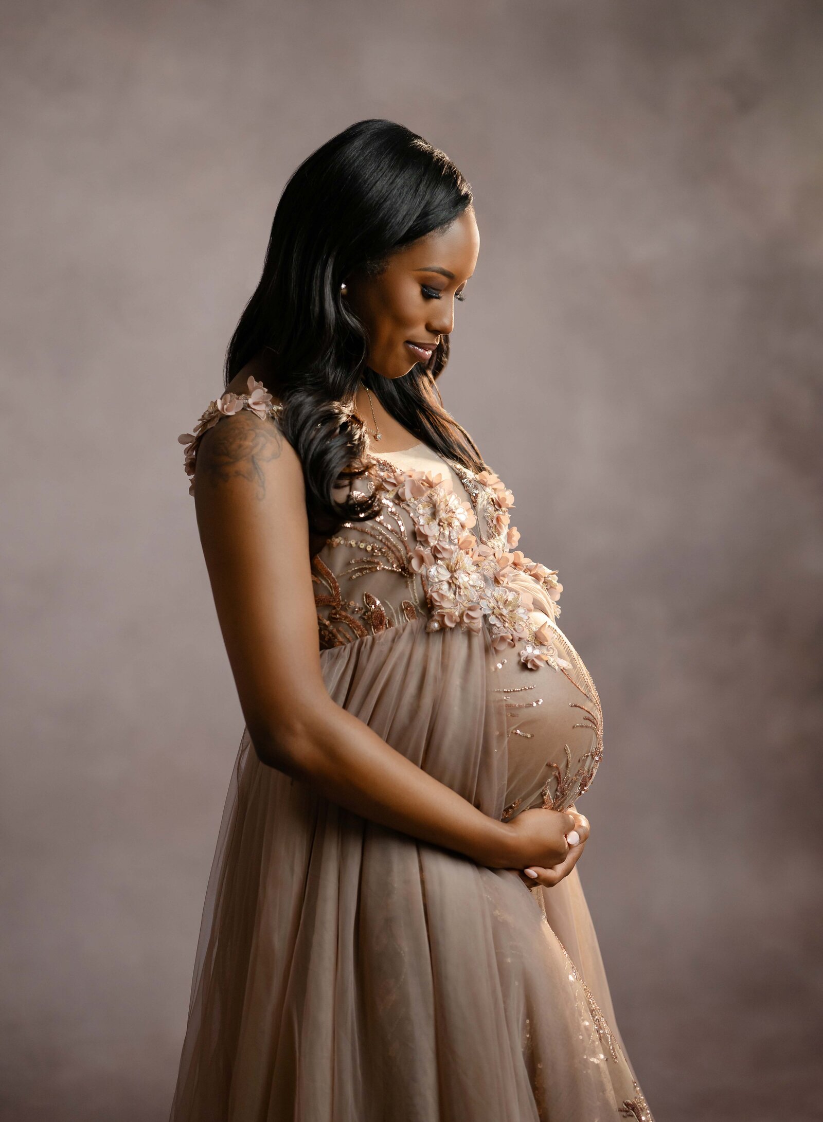 Pregnant women in rose gold gown, looking down at baby bump and smiling. Photo taken in Atlanta.