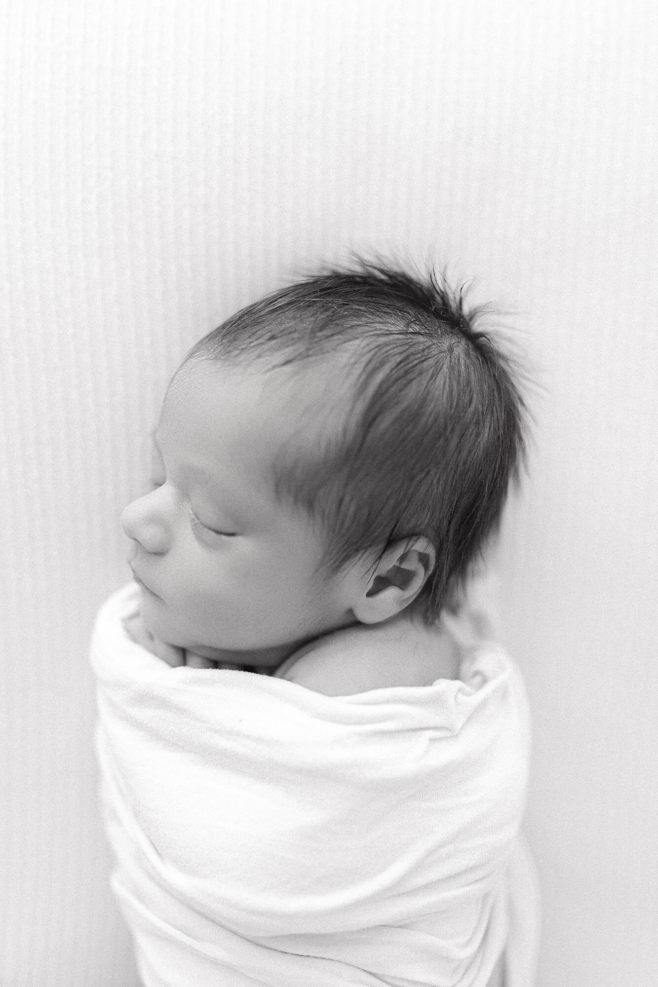 Sleeping newborn baby boy curled up in swaddle on white blanket | Grand Forks ND newborn photographer