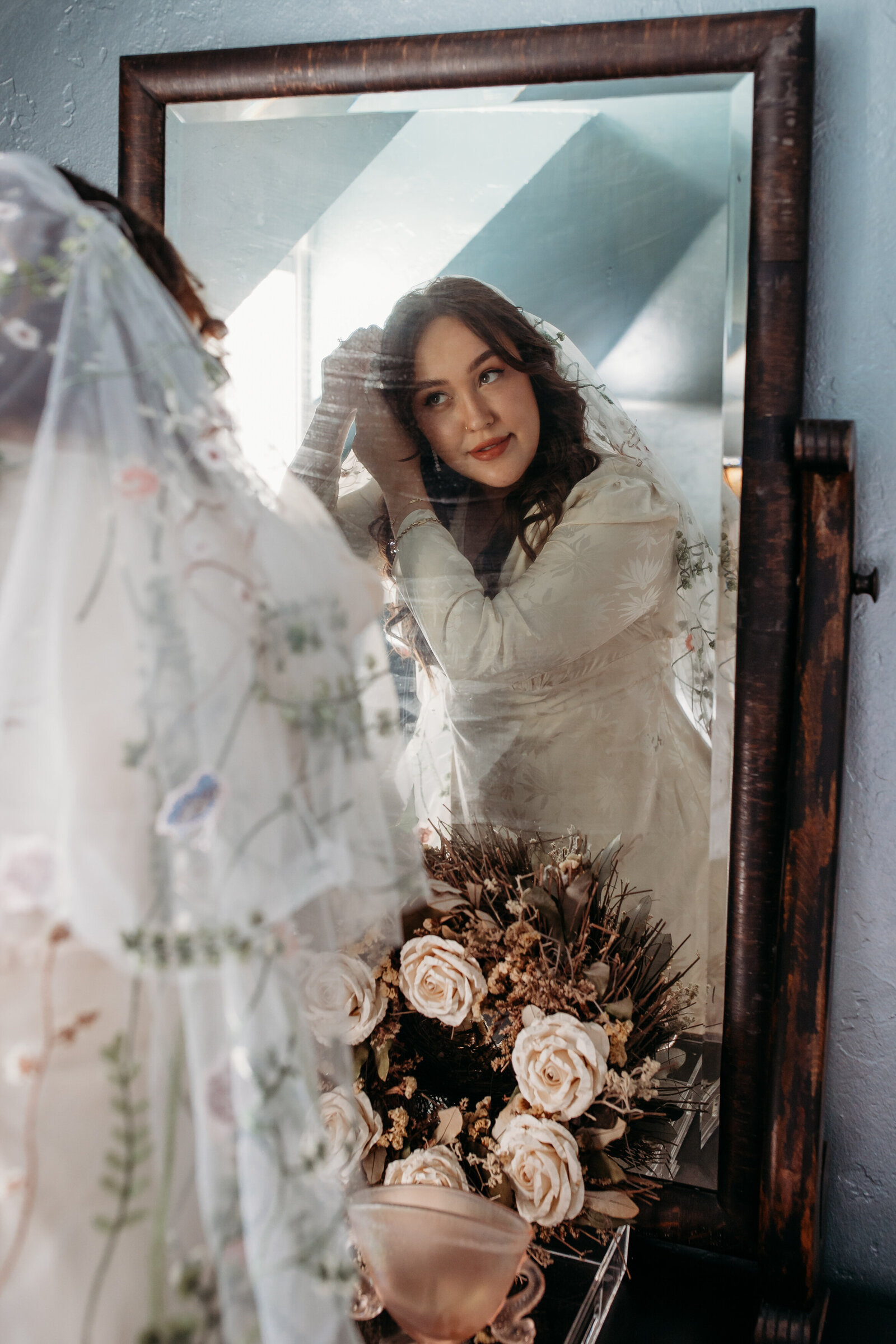 A bride in a detailed gown admires her reflection in a vintage mirror