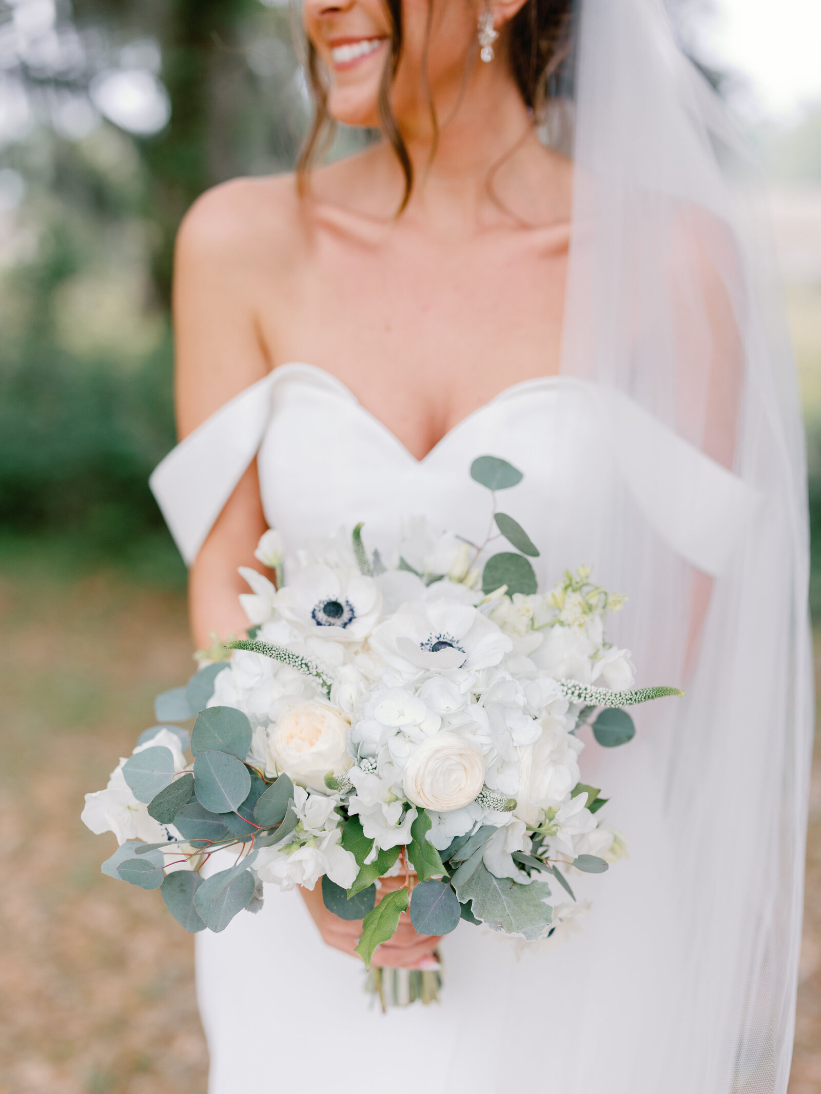 A bride and her bouquet with anemones, roses, ranunculus, and eucalyptus at her private estate wedding in Charleston, SC