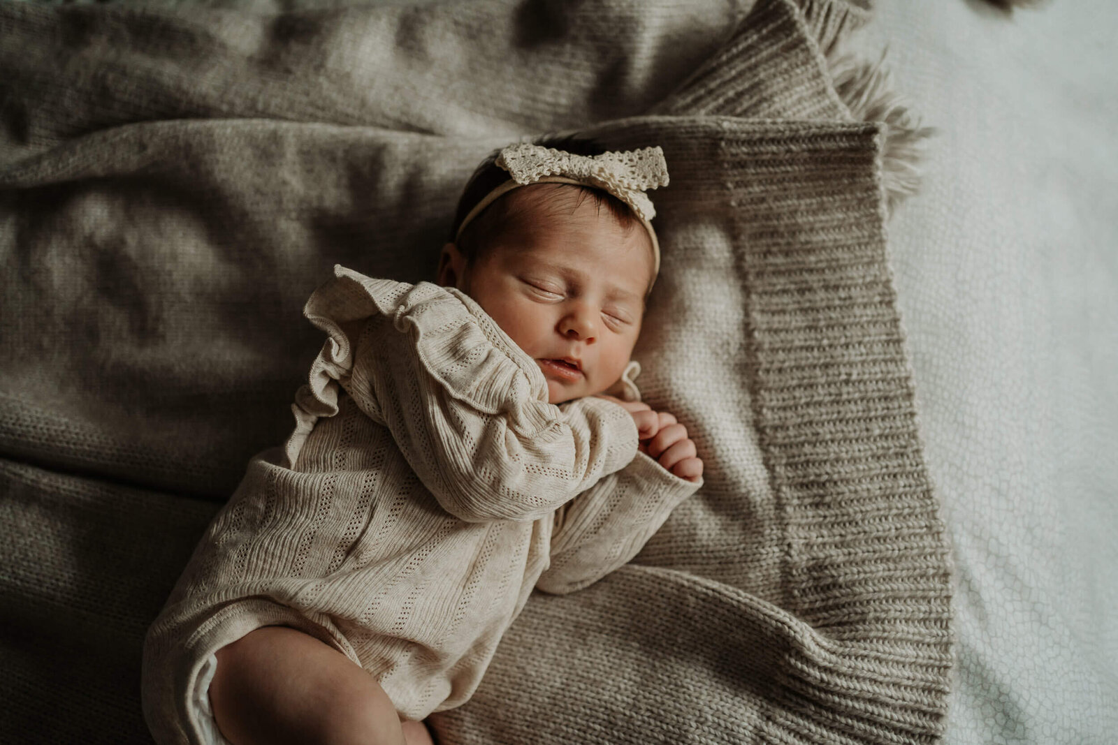Newborn baby girl with beige knit bowsleeping on a bed with beige blankets