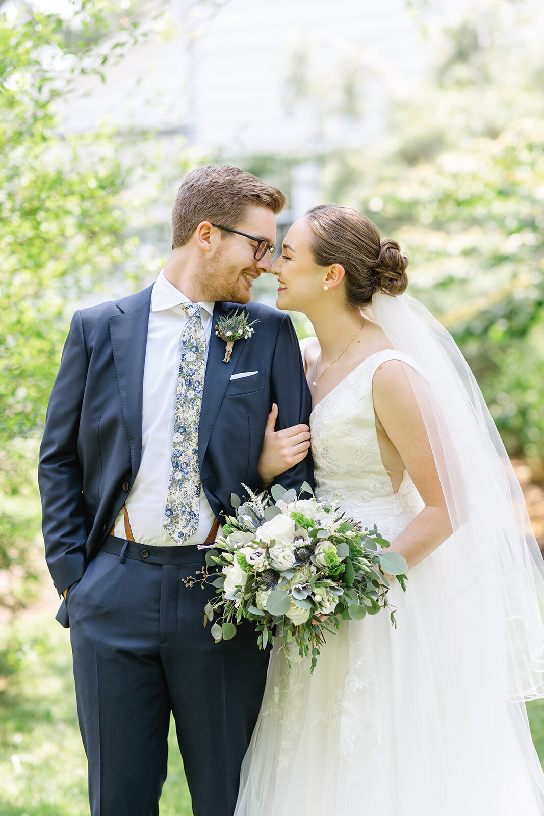Bride and groom touching foreheads on a garden lawn, the bride holding a white and green bouquet