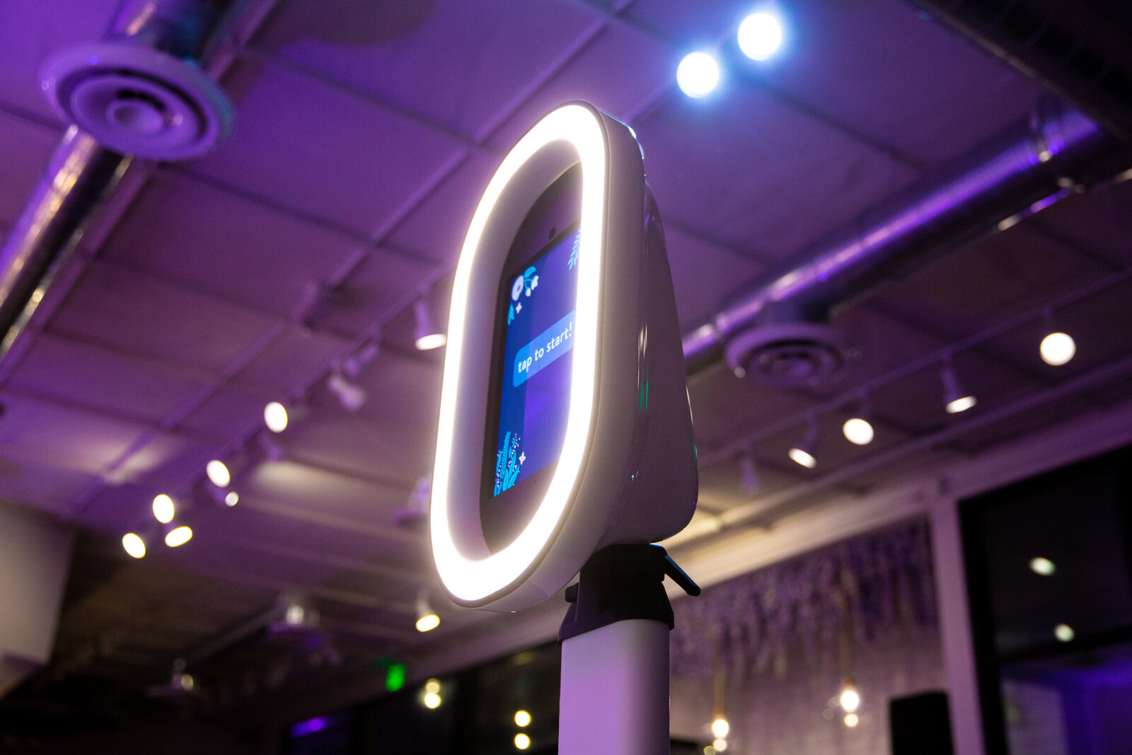 Modern photo booth glowing with a white ring light in a dimly lit event space, creating a sleek and moody vibe