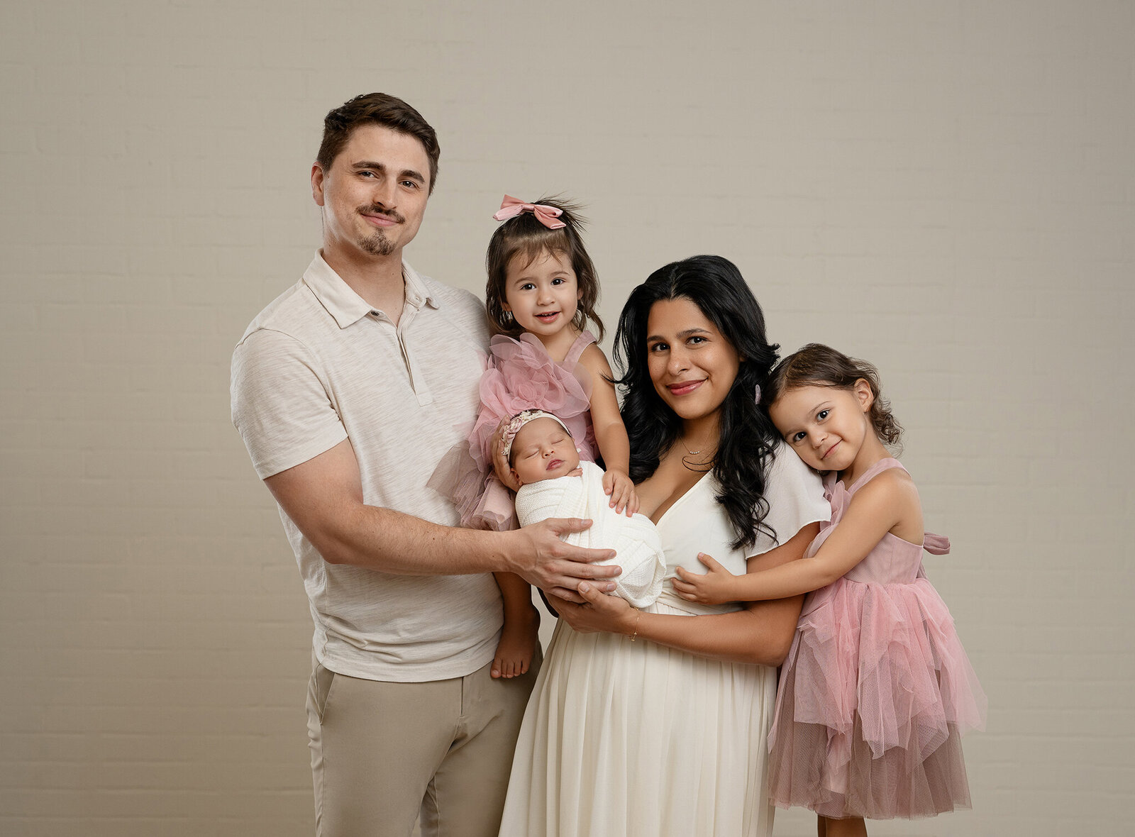 Mom holding newborn baby girl with older sister leaning on Mom and Dad holding middle sister. 
