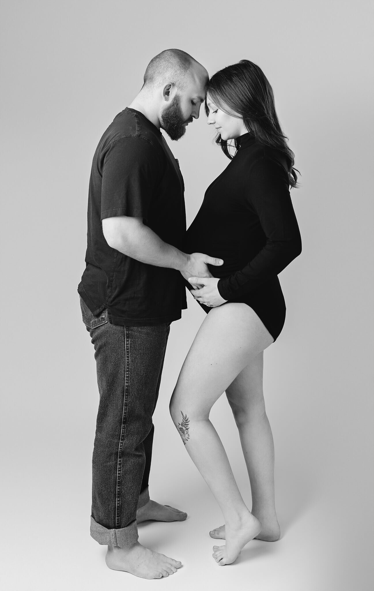 beautiful portrait of a couple expecting their first baby, he is wearing jeans and a black tshirt, she is wearing lingerie