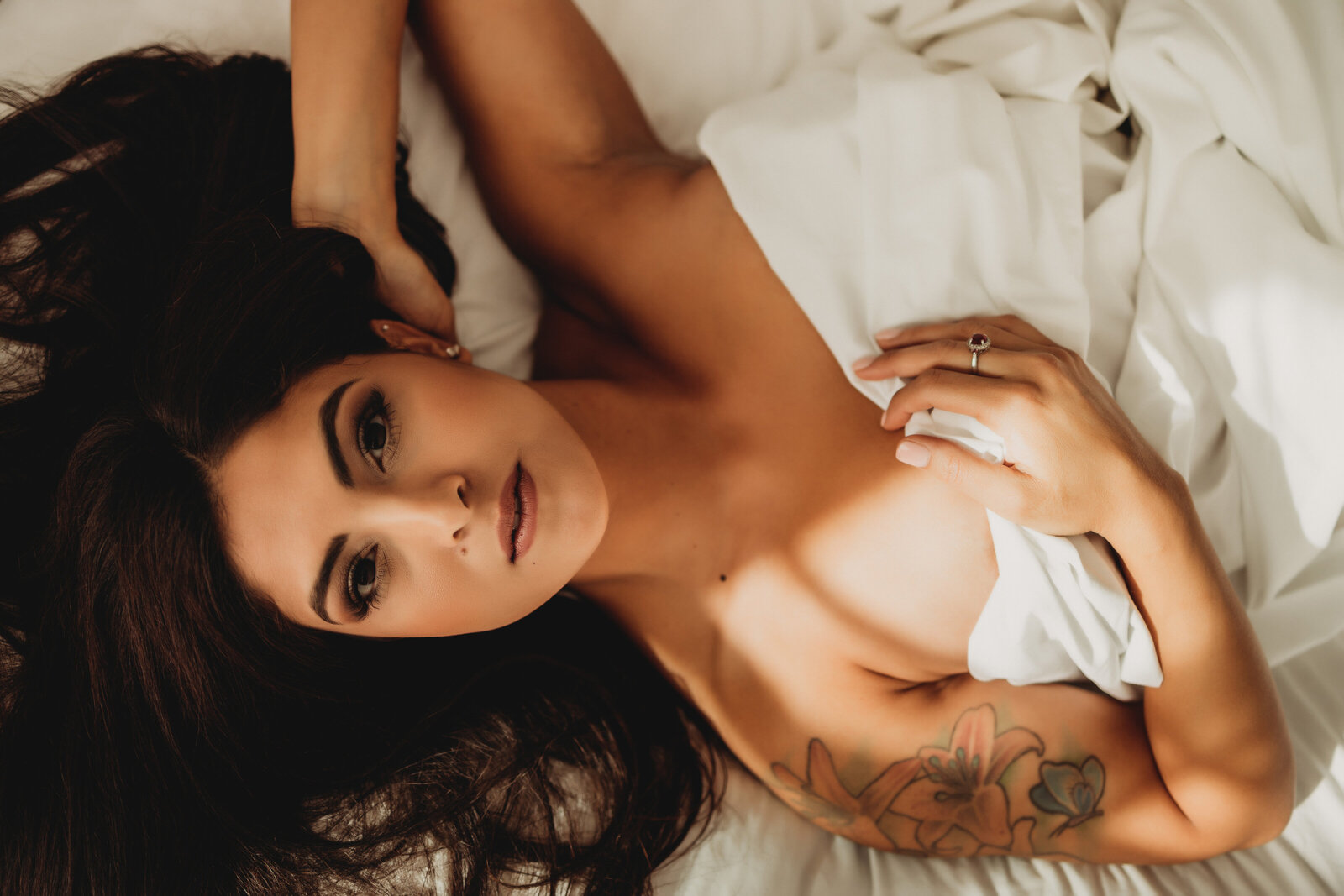 overhead photo of female laying in white sheets with beautiful hair and makeup for boudor photos