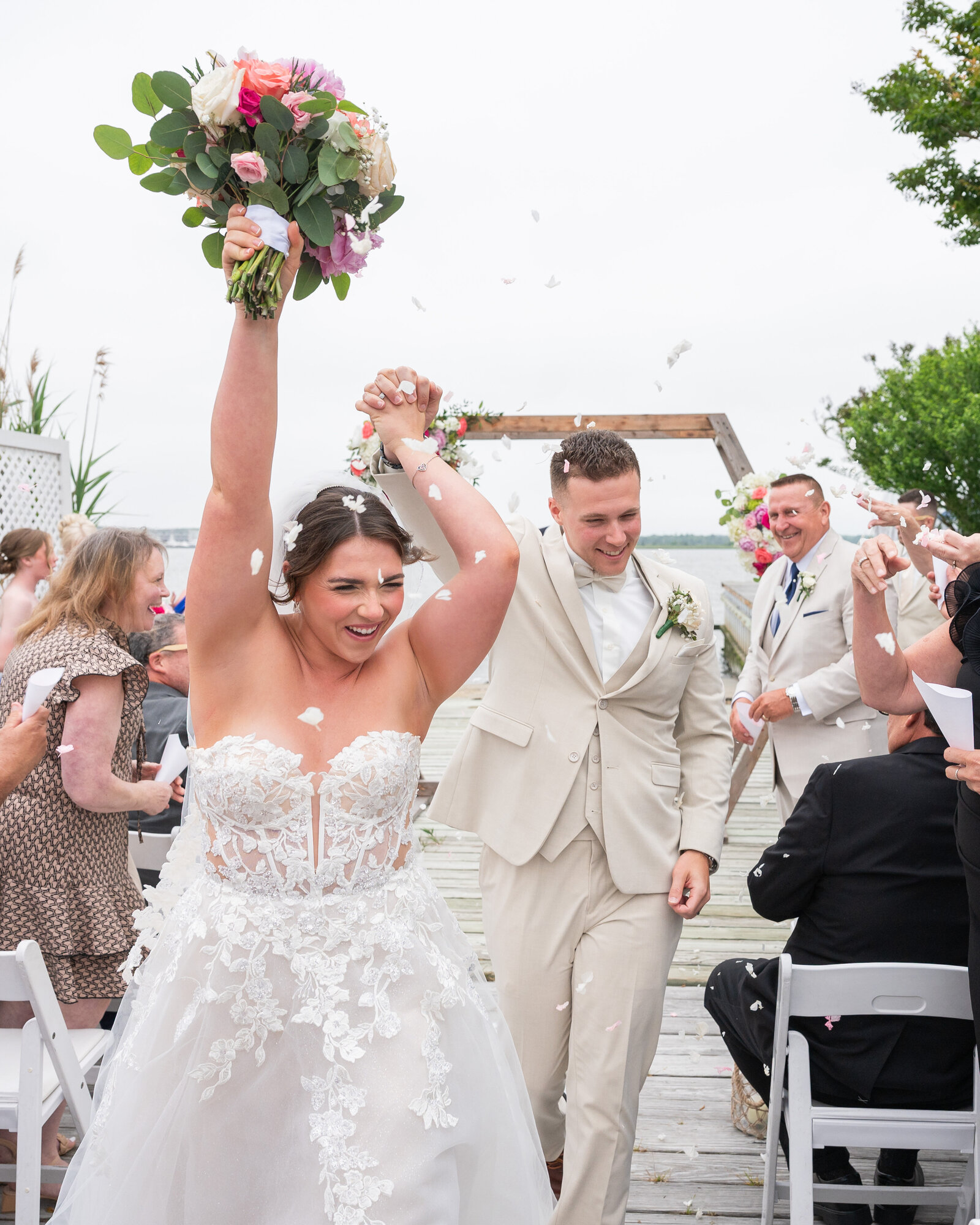 Bride and groom holding hands after getting married holding flowers in their hand and petals being thrown in the air
