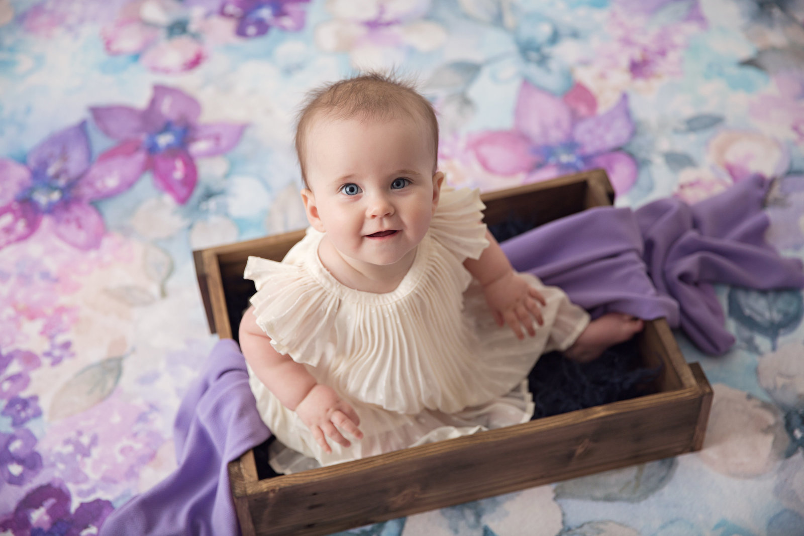baby girl sitting in crate purple flowers