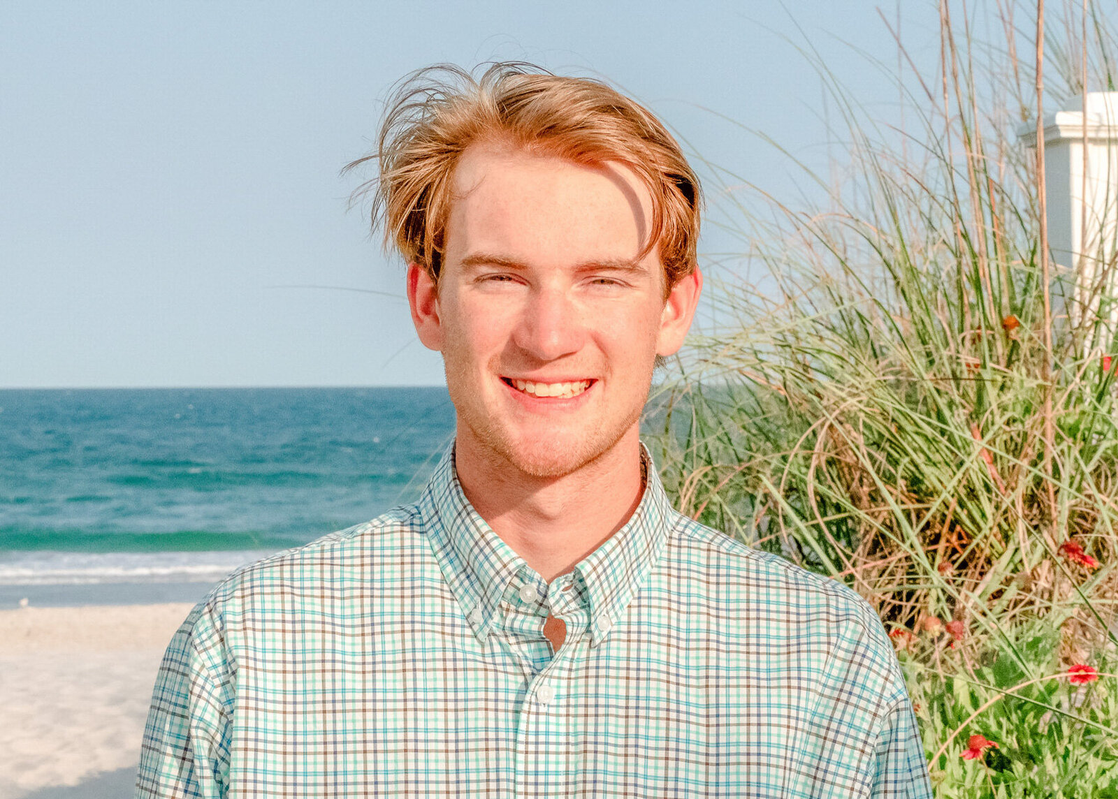  A high school senior smiling on Wrigthsville Beach with the ocean and dune grass in the background in North Carolina. This vibrant portrait exemplifies casual and natural senior photography, ideal for capturing youthful spirit.
