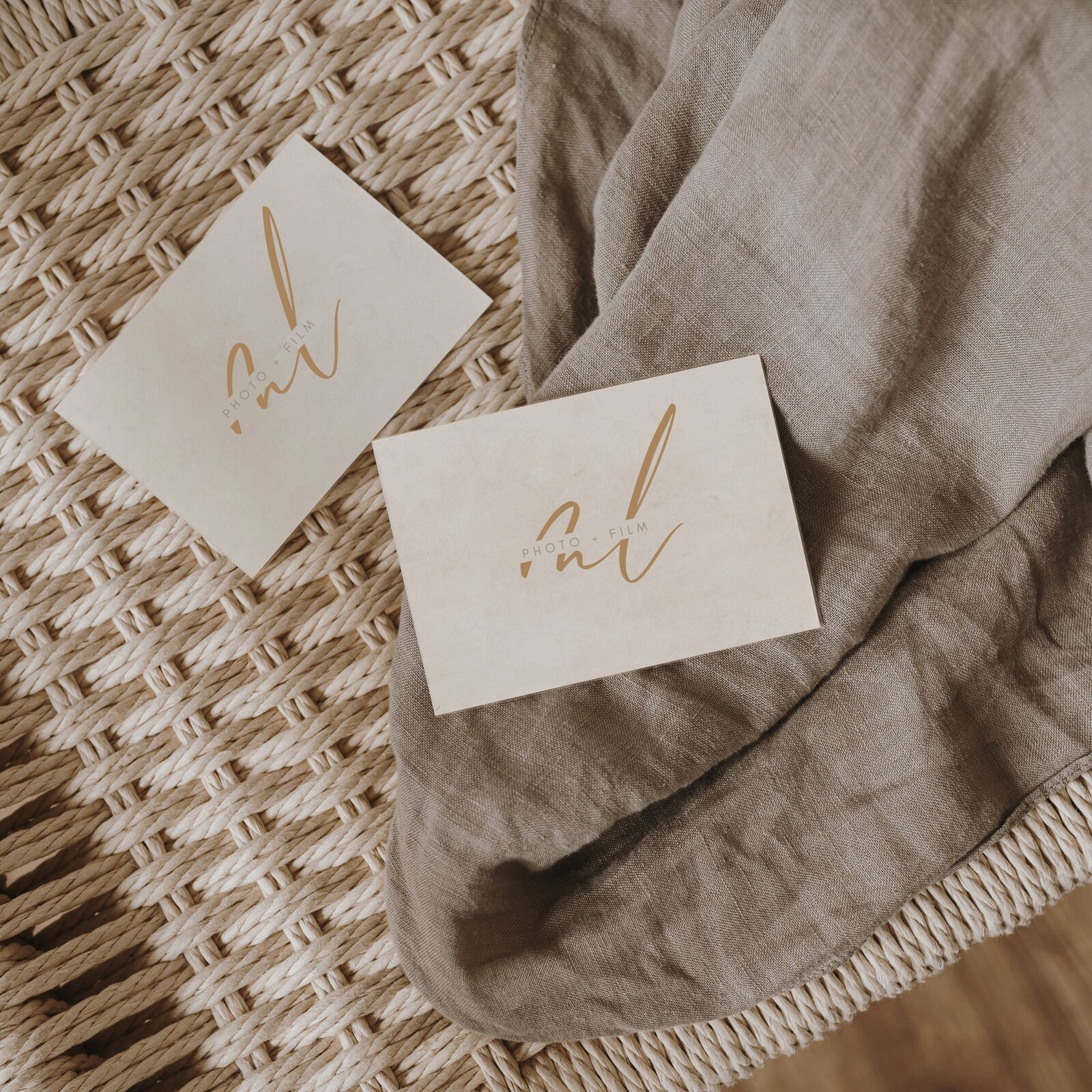 Two business cards with gold lettering placed on a woven surface partially covered by a gray fabric.