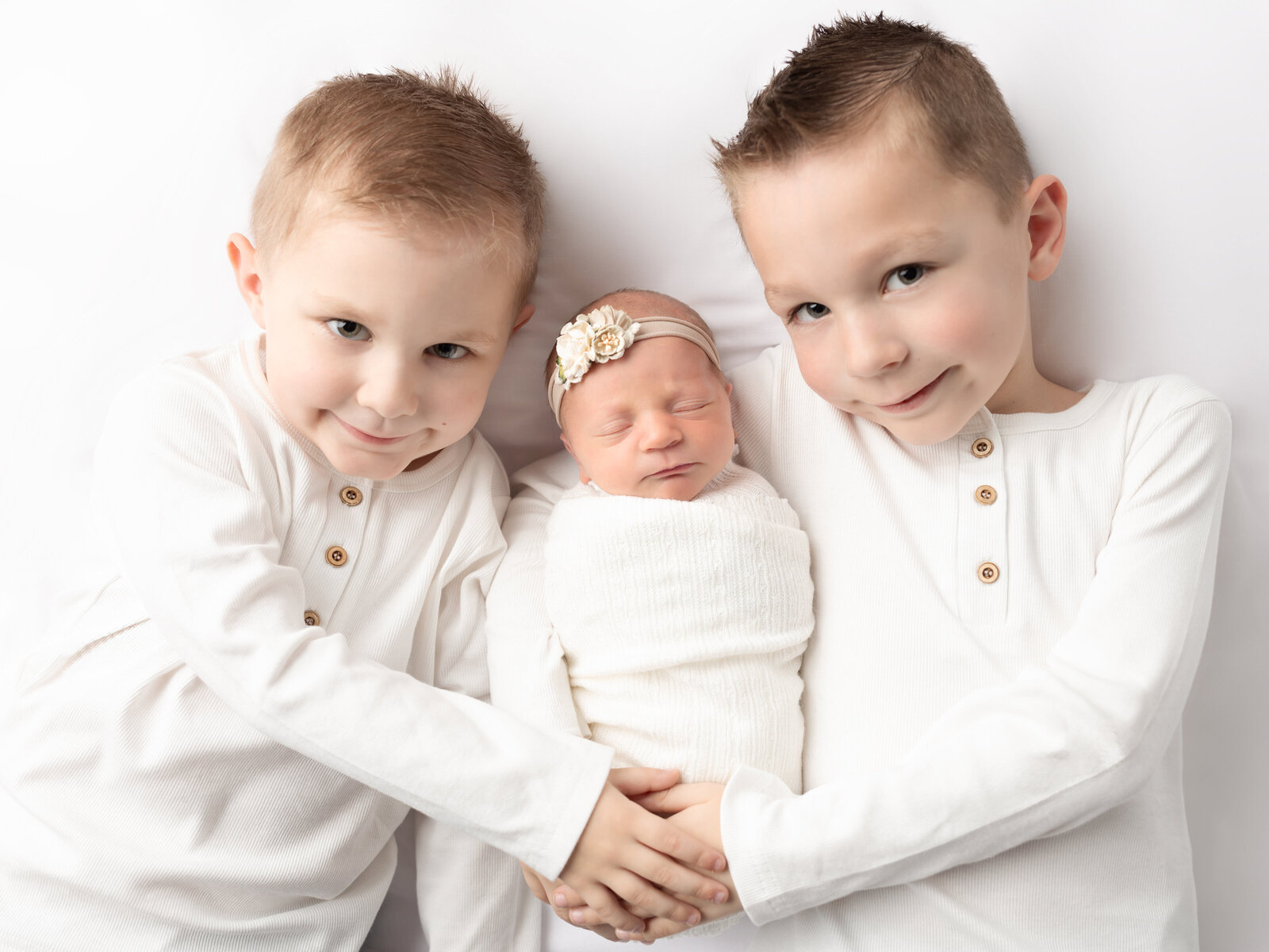 brothers holding newborn baby sister for photoshoot