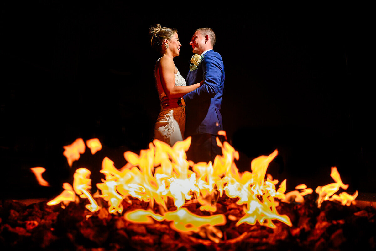 A wedding couple stands in front of a fire at Jay Peak Resort in Vermont, captured by Eaton Photo