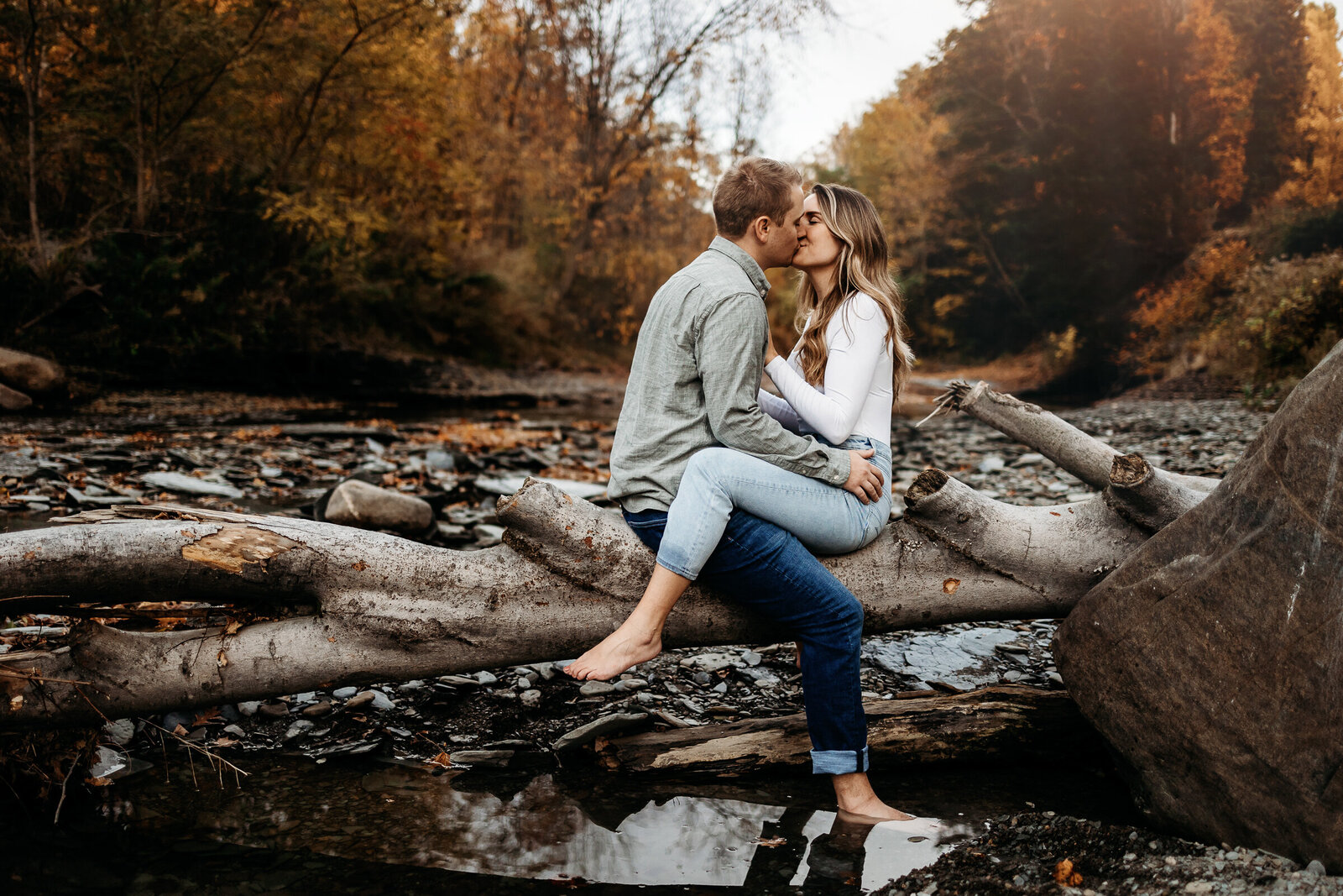 Couple shares a passionate kiss while sitting on a log  stretched across a tranquil stream