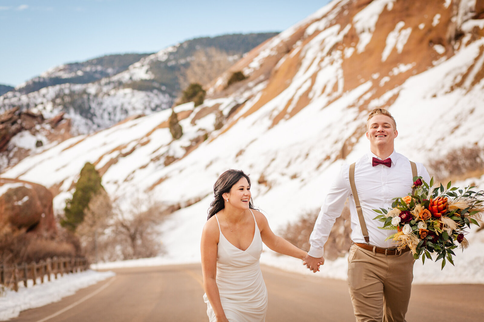 Bride and groom run down the road while holding hands
