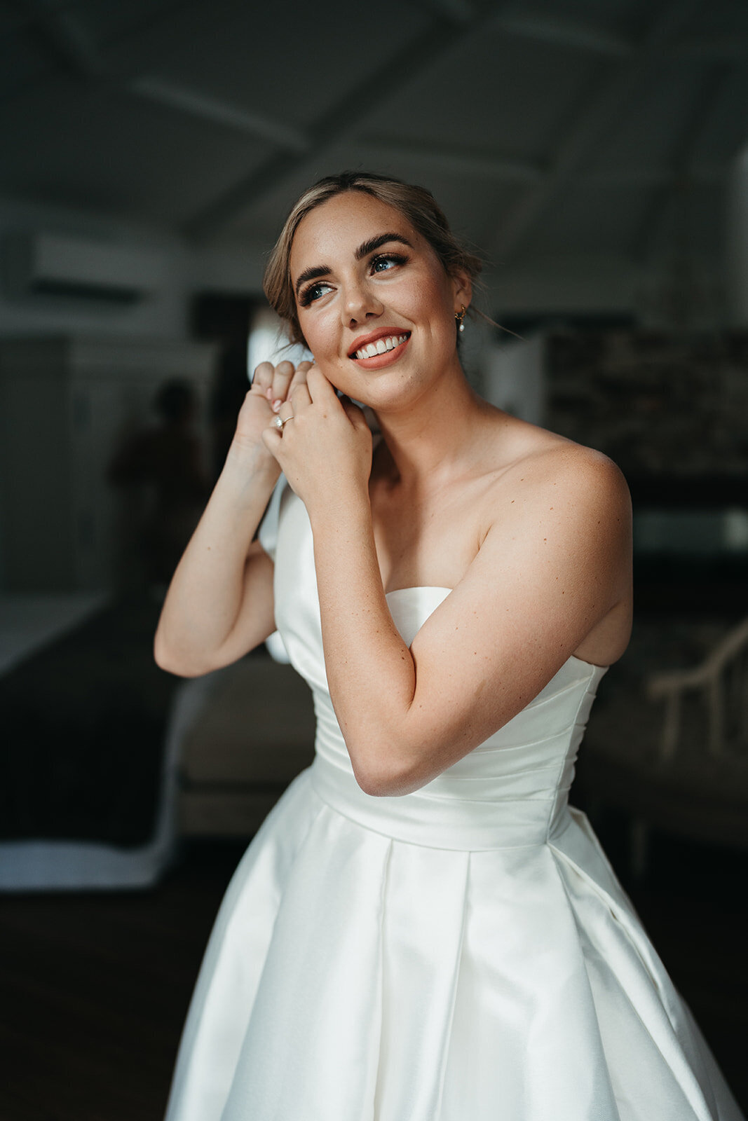 Gorgeous Bella Rae Bride Kristen putting her earrings on looking stunning with bronzy eye and peachy lip amd low textured twisted bun