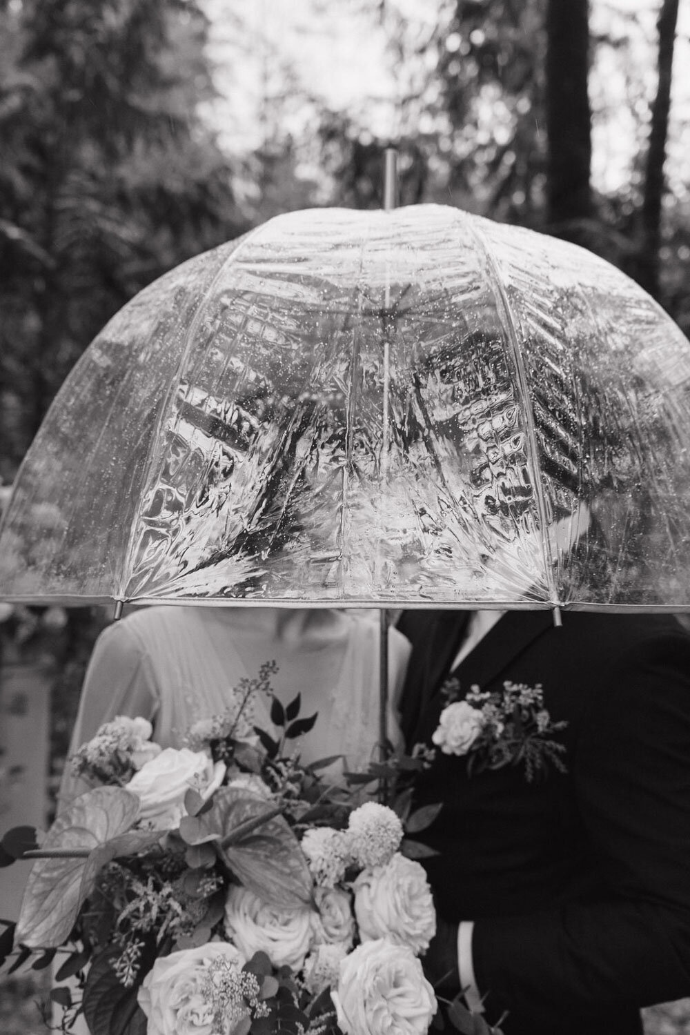 Bride and groom under a clear umbrella in a forest setting